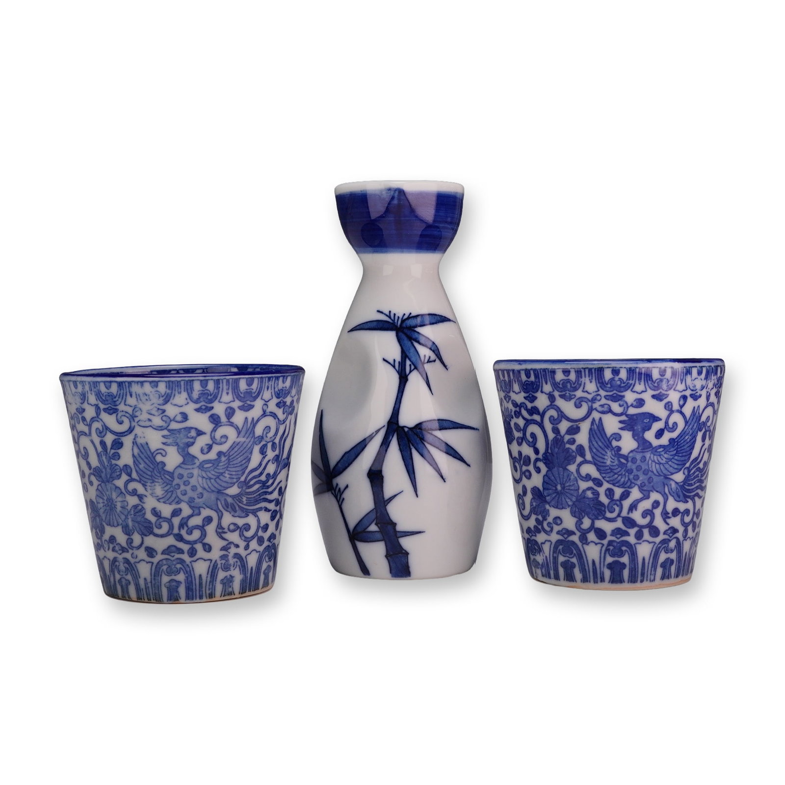 Three-piece Japanese Blue and White Porcelain Sake Set with Bamboo and Phoenix Motifs: This three-piece Japanese sake set is crafted from porcelain and decorated with vibrant underglaze blue. The set includes one tokkuri (flask) and two choko (cups). The tokkuri features an ovoid body w
