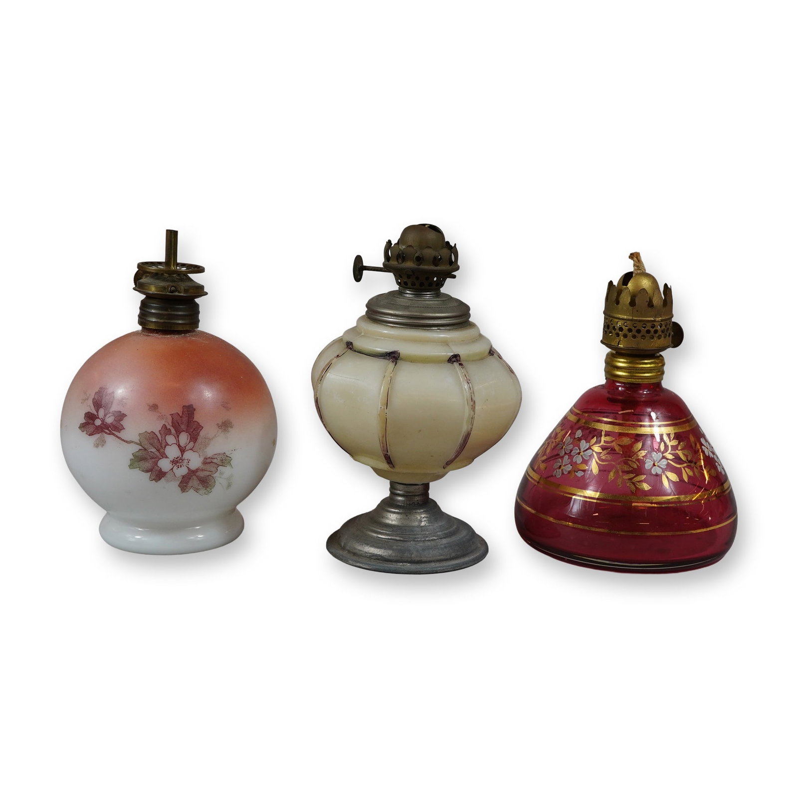 3pc Antique Miniature Glass Oil Lamps Including Cranberry and Milk Glass: This collection features three antique miniature oil lamps, often known as night or courting lamps, originating from the late 19th to early 20th century. The first lamp is made of milk glass with a pe
