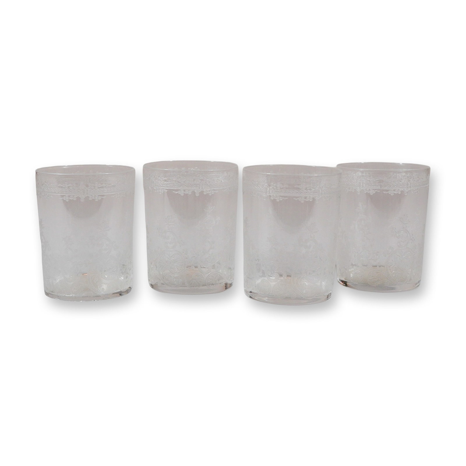 Set of Four American Etched Glass Small Flat Bottom Tumblers: A set of four clear glass tumblers featuring intricate needle-etched decoration. Each vessel is designed with a cylindrical form and a flat bottom. The exterior is decorated with a primary band of etc