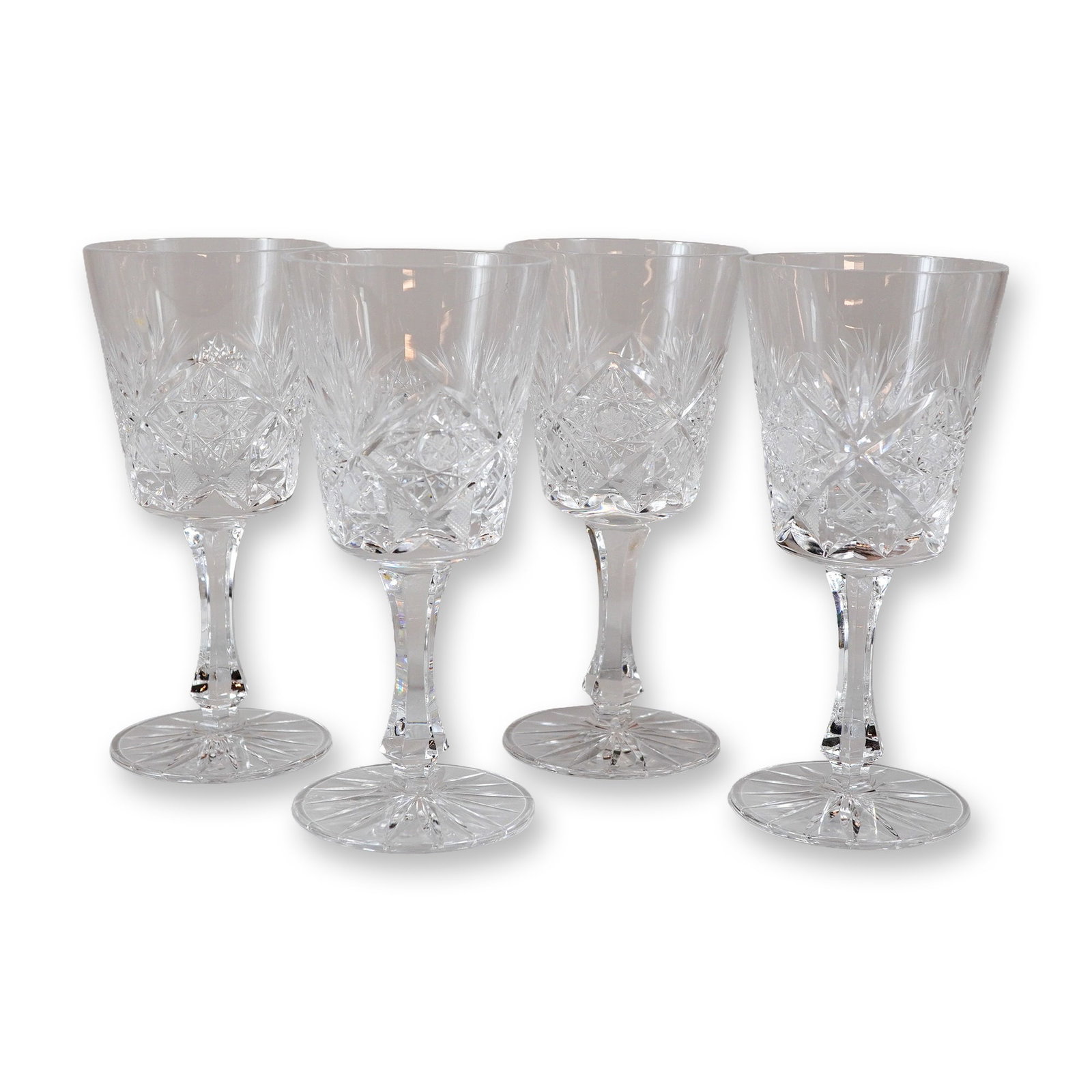 Set of Four Cut Crystal Stemware Glasses in the Star and Fan Pattern: This set of four crystal glasses features a deep, slightly tapered cylindrical bowl decorated with a complex geometric pattern. The design includes a central band of large rosettes with crisscrossed c