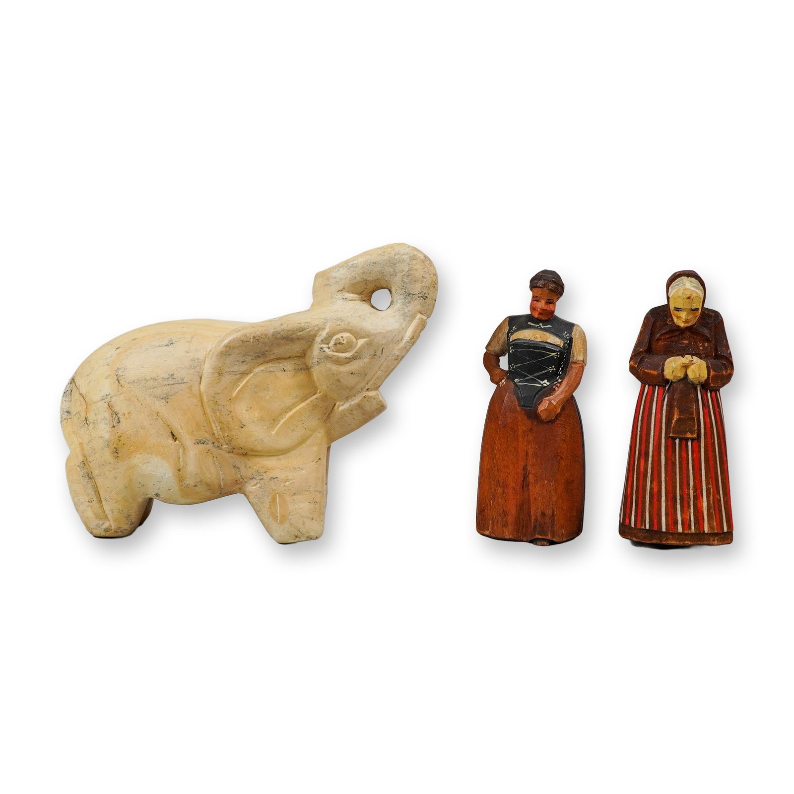 3pc Carved Figurines, Two Painted Wood Female Figures and One Stone Elephant: This lot consists of three small decorative figurines. Included is one elephant figurine carved from a light-colored stone, such as alabaster or soapstone, showing natural gray and yellow veining.