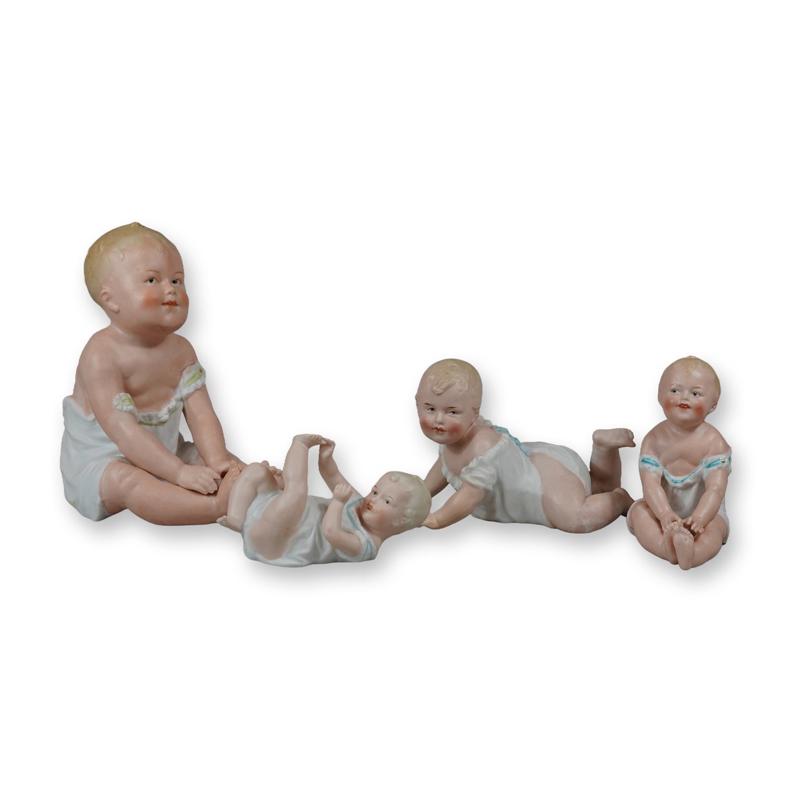 4pc German Bisque Porcelain Piano Babies: A lot of four German bisque porcelain piano baby figurines manufactured by Gebruder Heubach. The collection includes four infants in various lifelike poses: one large sitting baby looking to the side,