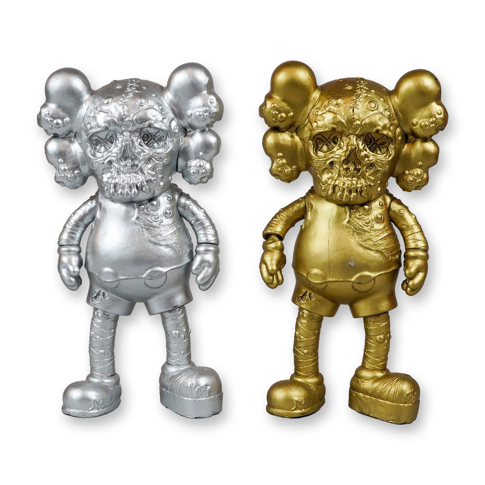 2pc KAWS x Pushead Companion Crossover Figures: This lot features two unmarked plastic figures depicting the KAWS x Pushead companion crossover character. One figure is finished in a metallic silver tone and the other in a metallic gold tone. These