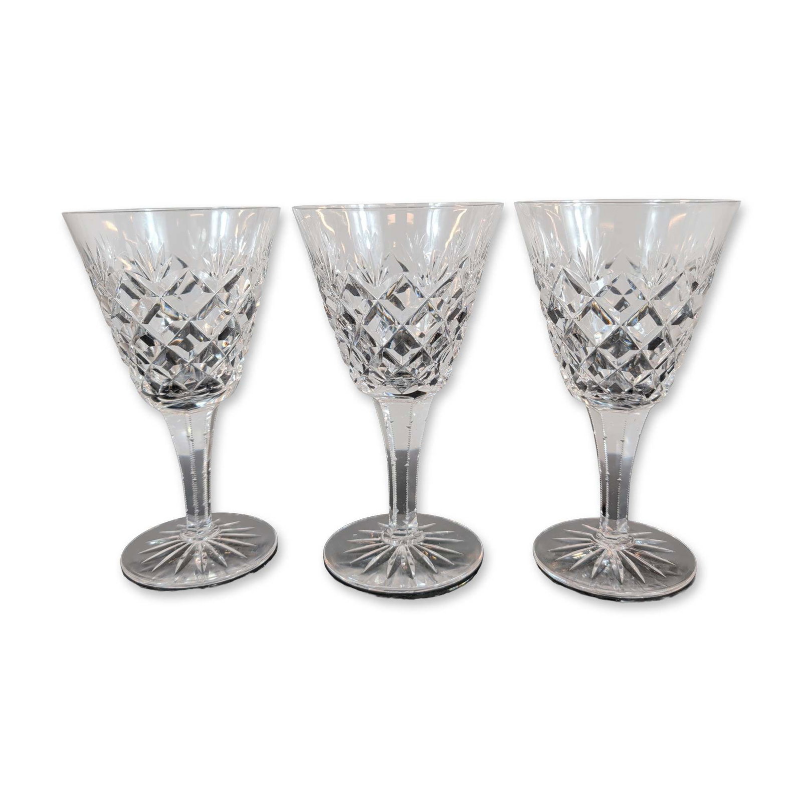 Trio of Crystal Goblets: Three goblets featuring hand-cut criss-cross diamond patterns on the lower bowl transitioning to vertical wedge cuts at the rim. The faceted stems taper to a circular foot with a sixteen-point radial