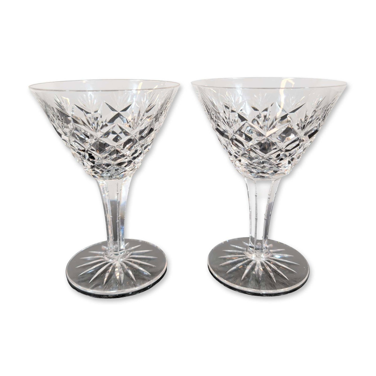 2pc Cut Crystal Coupes: A pair of cut crystal glasses. Each glass is crafted from heavy lead crystal featuring a cross-hatched diamond-cut lower bowl surmounted by upward-pointing wedge cuts. The multisided stem is finished