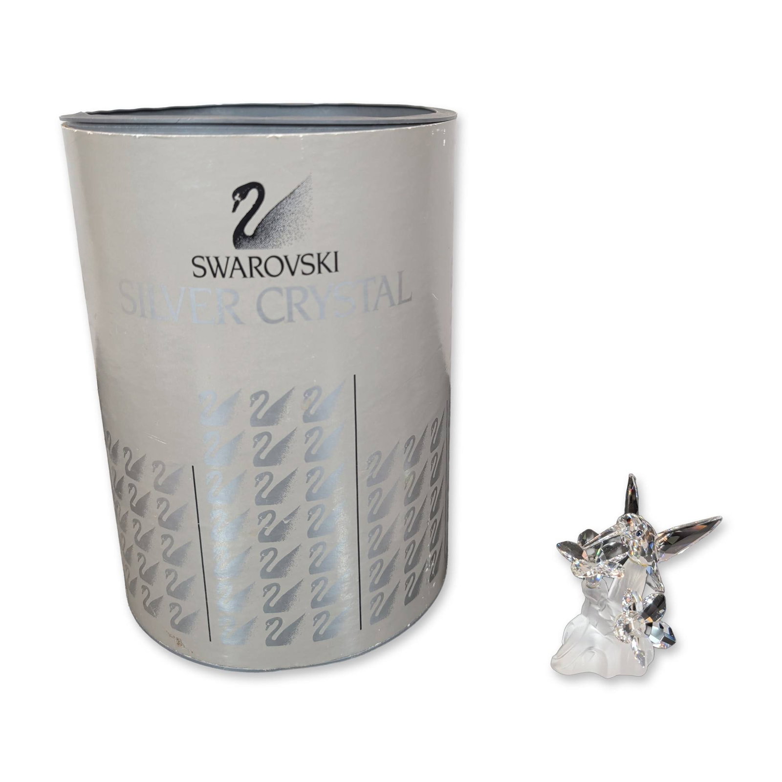 Swarovski Silver Crystal Hummingbird with Flowers: The piece is crafted in faceted clear lead crystal, depicting a hummingbird with dark blue crystal eyes hovering over two blossoms. The scene is mounted on a wave-like frosted crystal base. Swarovski 