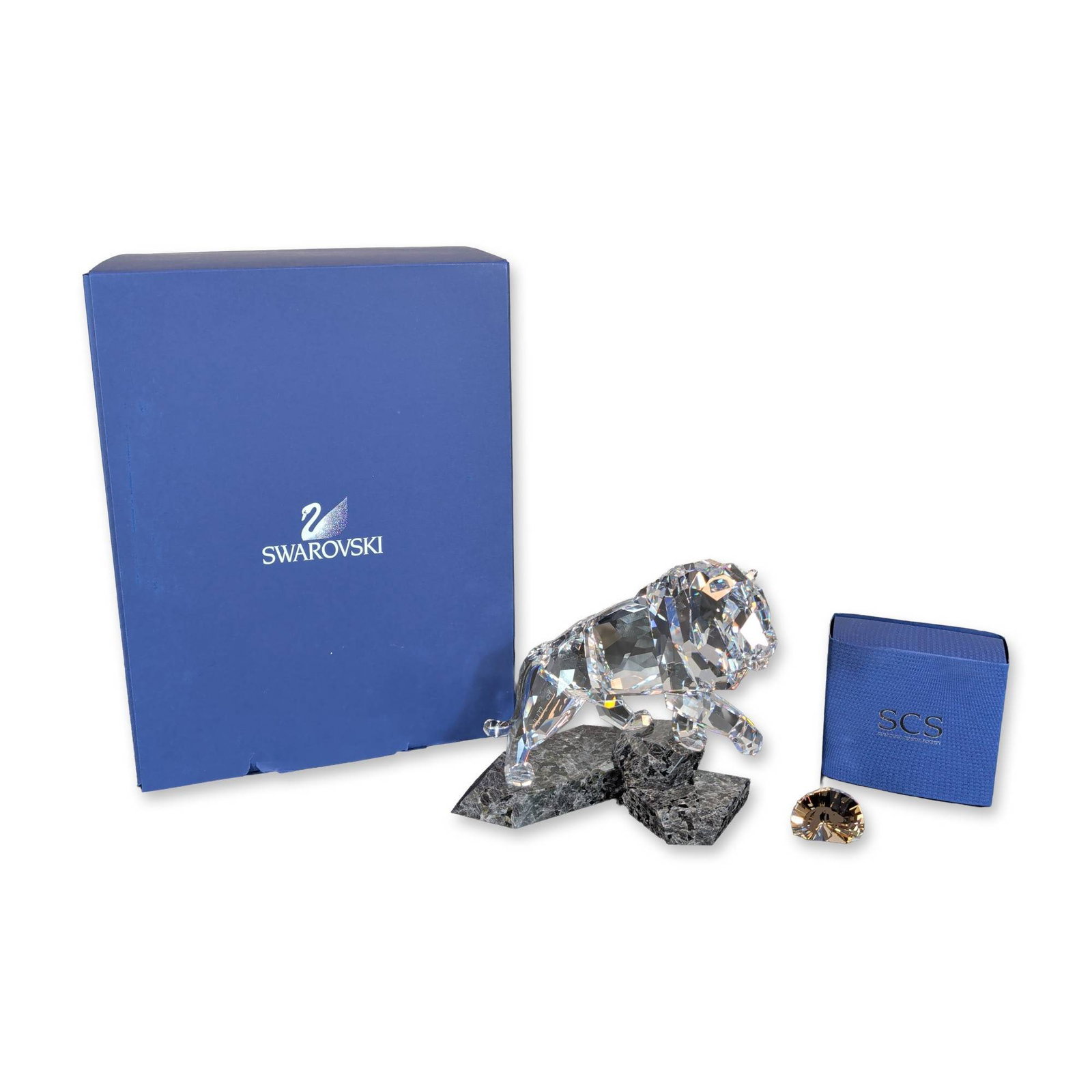 2pc Swarovski Crystal The Brave and Proud Lion Figurine with Plaque: Faceted clear lead crystal lion in a pouncing pose, mounted to a granite dark gray and black crystal base resembling natural rock. The lot includes the original blue Swarovski presentation box, a smal