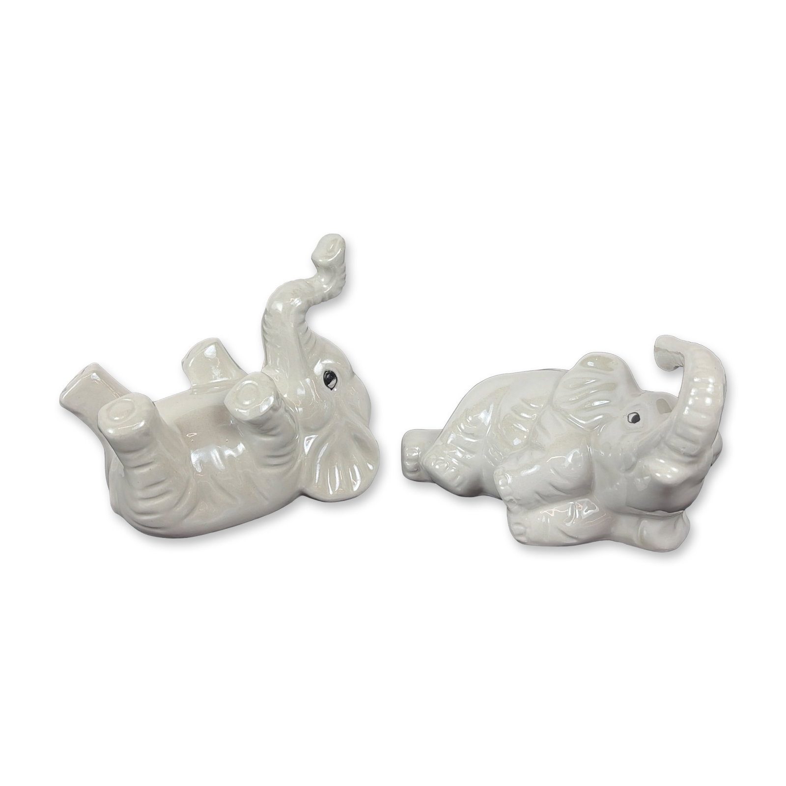 Pair of Brazilian Lusterware Porcelain Elephant Figurines: Brazilian. Pair of baby elephant figurines in white iridescent lusterware glazed porcelain. Each figurine is modeled in a distinct pose with painted black eyes; one elephant features a raised trunk wh