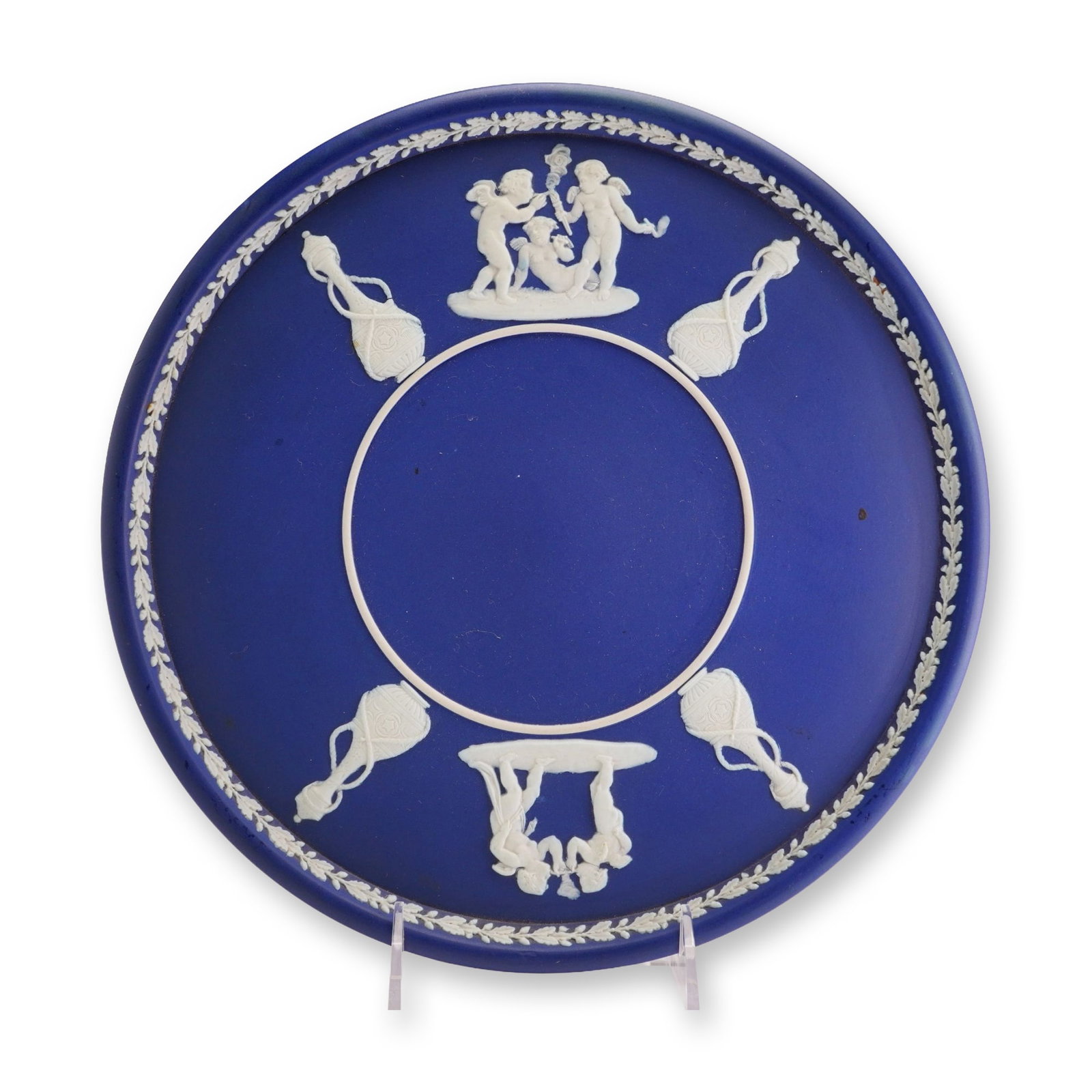 Wedgwood Blue Jasperware Classical Motif Underplate: This circular underplate is manufactured by Wedgwood in blue jasperware, an unglazed stoneware with a matte finish. The piece features a cobalt blue ground with white sprigged bas-relief decoration. T