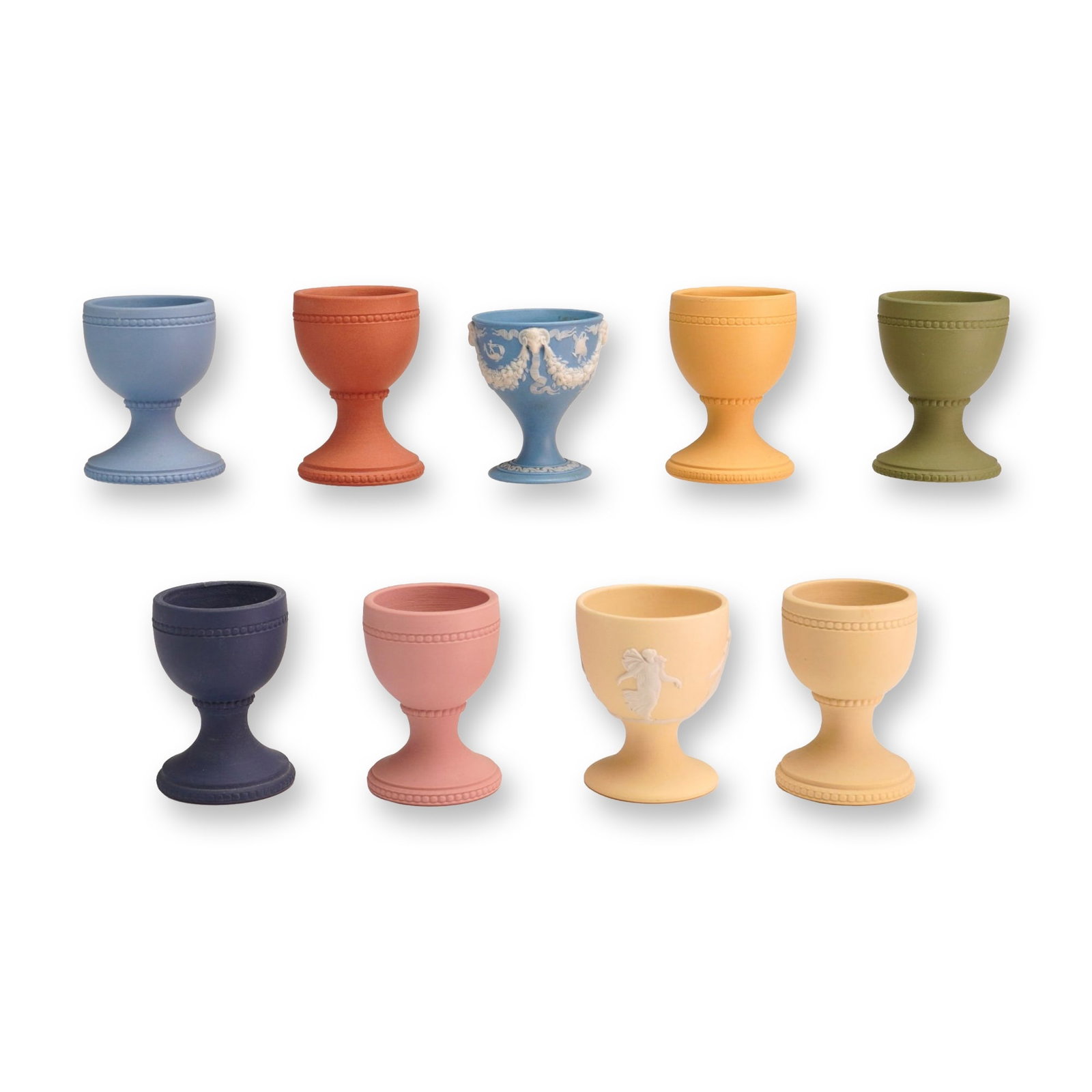 Nine Wedgwood Jasperware Miniature Eggcups: A collection of nine miniature pedestal-base eggcups crafted in fine-grained unglazed jasperware stoneware. The group includes seven solid-colored examples featuring embossed beaded borders around the