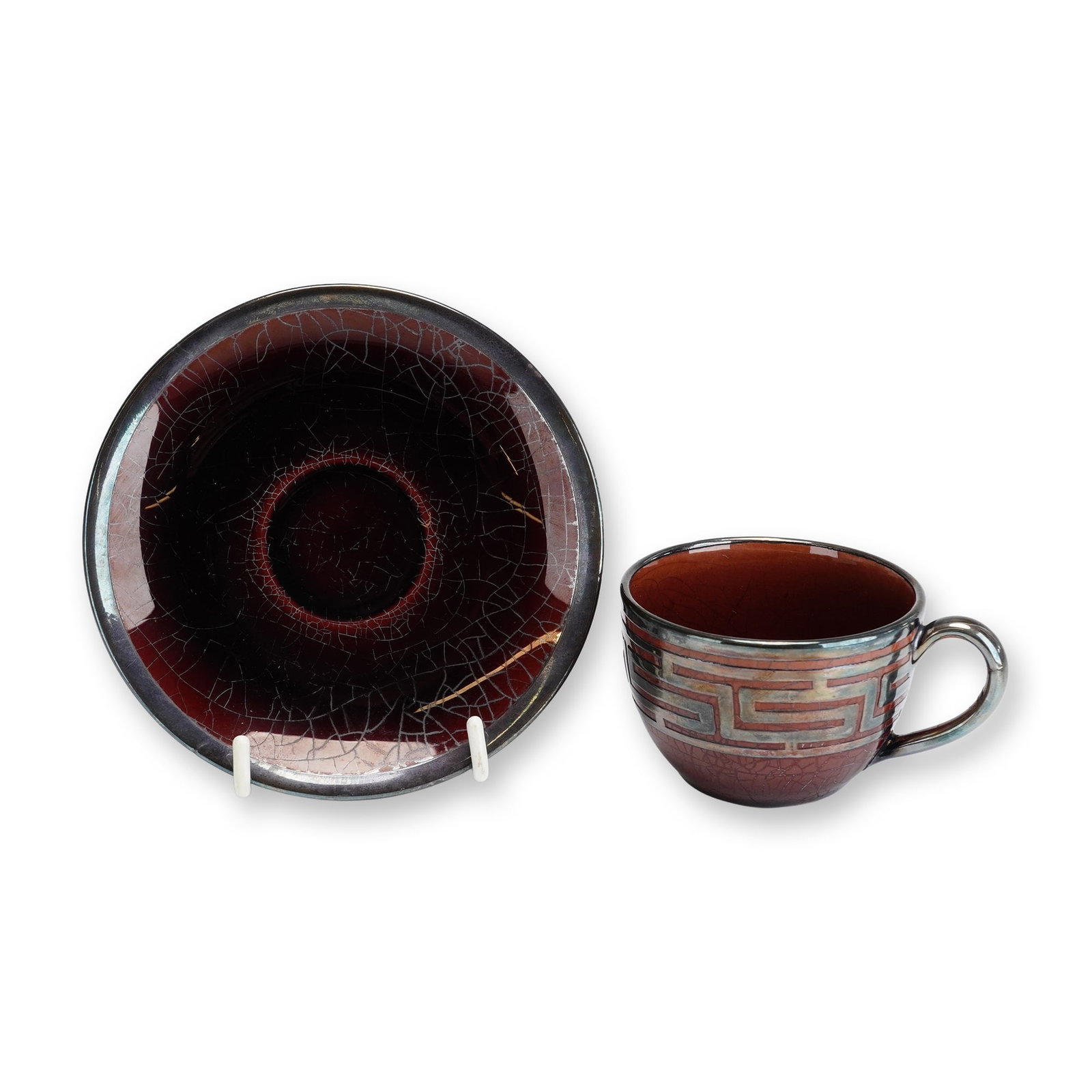 Wedgwood Crackle Glaze Cup and Saucer with Silver-toned Overlay: This two-piece ceramic set consists of a rounded tea or coffee cup and a matching shallow circular saucer. Both pieces are crafted from earthenware and finished in a deep oxblood or sang de boeuf-colo
