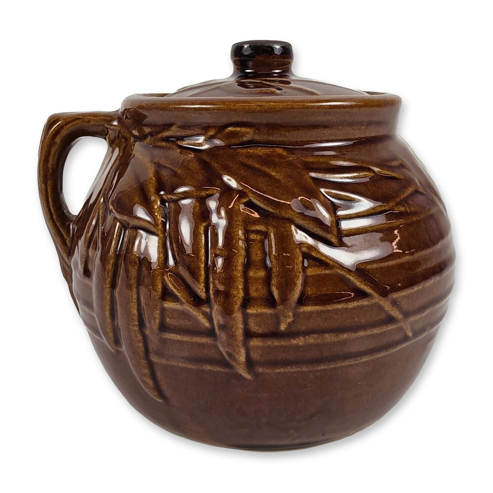 McCoy Brown Glazed Bamboo Leaf Jar: Lidded ceramic jar in brown glazed earthenware, featuring a relief-molded motif resembling bamboo leaves against a background of vertical and horizontal linear banding. The bulbous form includes a wid