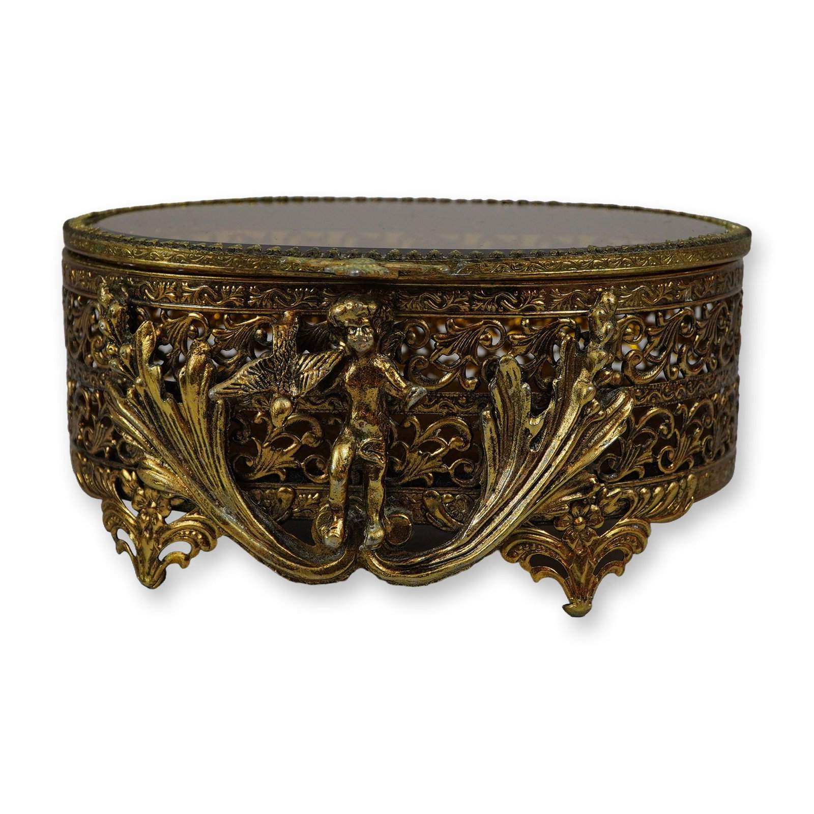Hollywood Regency Style Gilt Filigree Jewelry Box: Mid-20th century Hollywood Regency style oval jewelry box in gilt metal, featuring pierced filigree scrollwork sides. The front is embellished with a cast relief of a central putto flanked by large ac