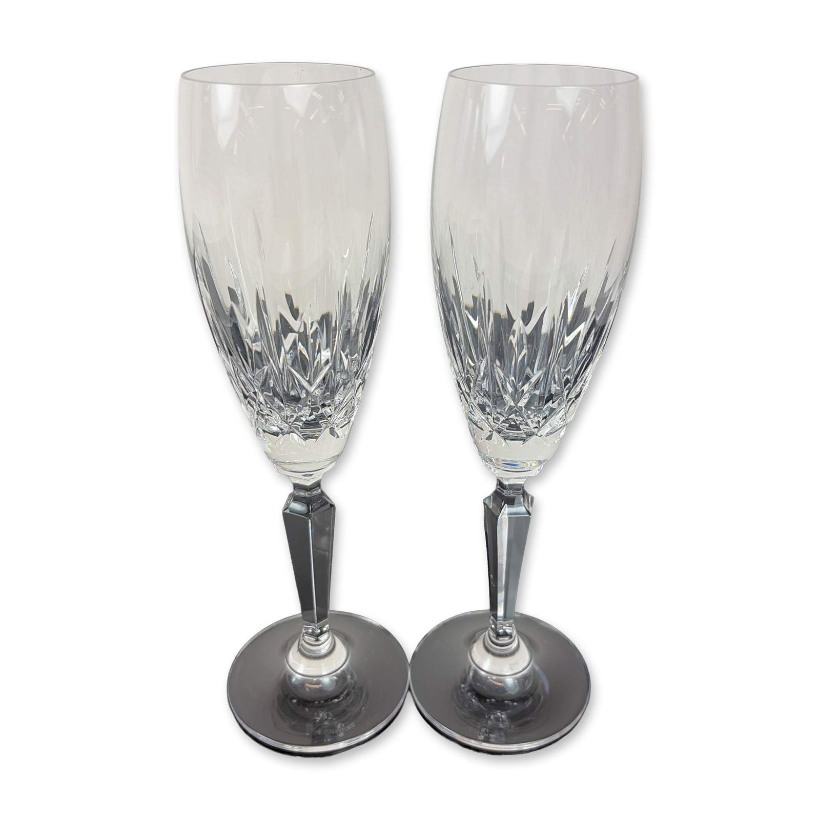 Pair of Waterford Lismore Crystal Champagne Flutes: Waterford. Champagne flutes in hand-cut lead crystal, featuring the Lismore pattern with deep vertical wedge cuts over a band of diamond-cut cross-hatching. Each glass is designed with a multi-faceted