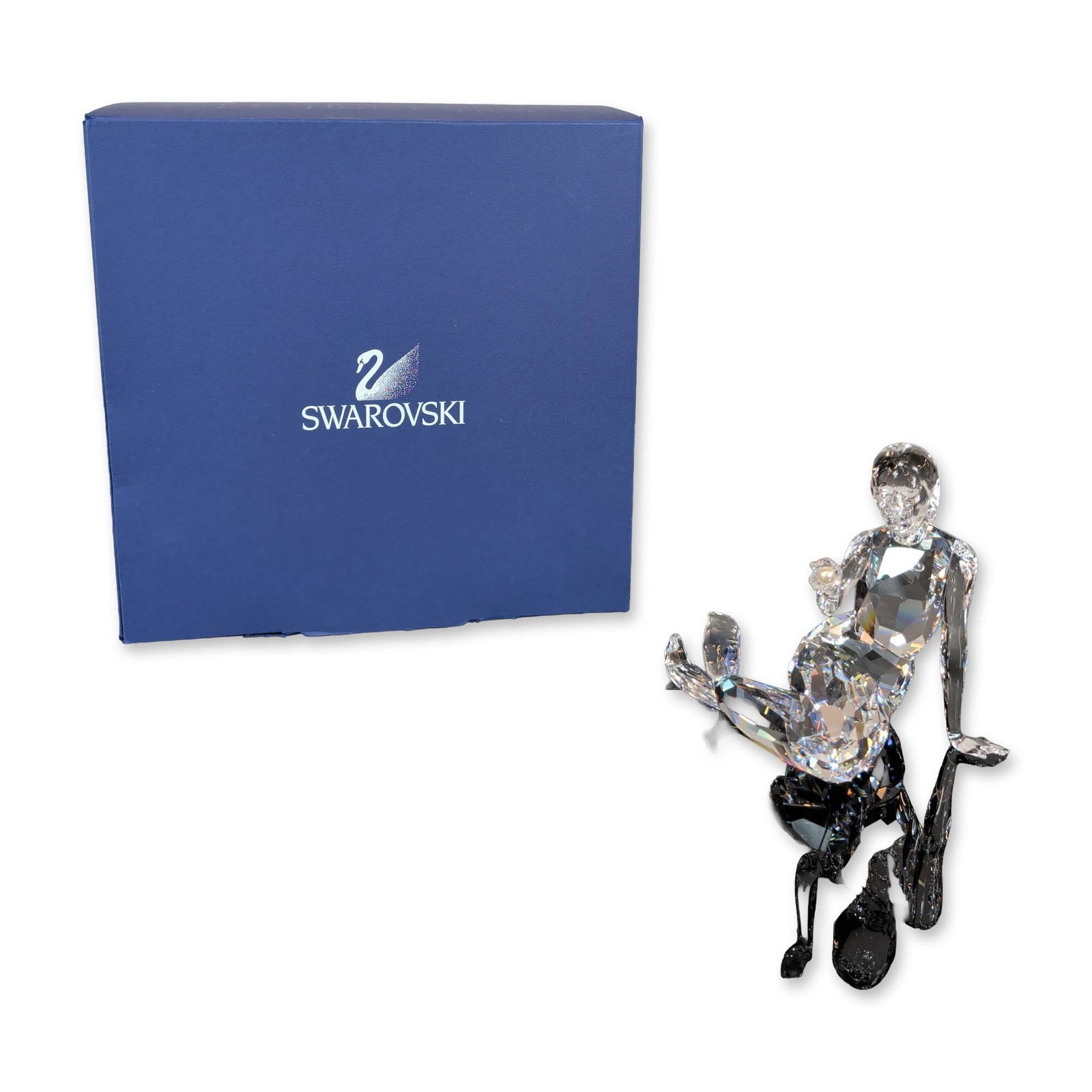 Swarovski Crystal Mermaid Figurine: Swarovski. Figurine in faceted clear lead crystal, depicting a mermaid in a seated pose leaning back. Features geometric faceting and a small white pearl accent held in the right hand. Etched Swarovsk