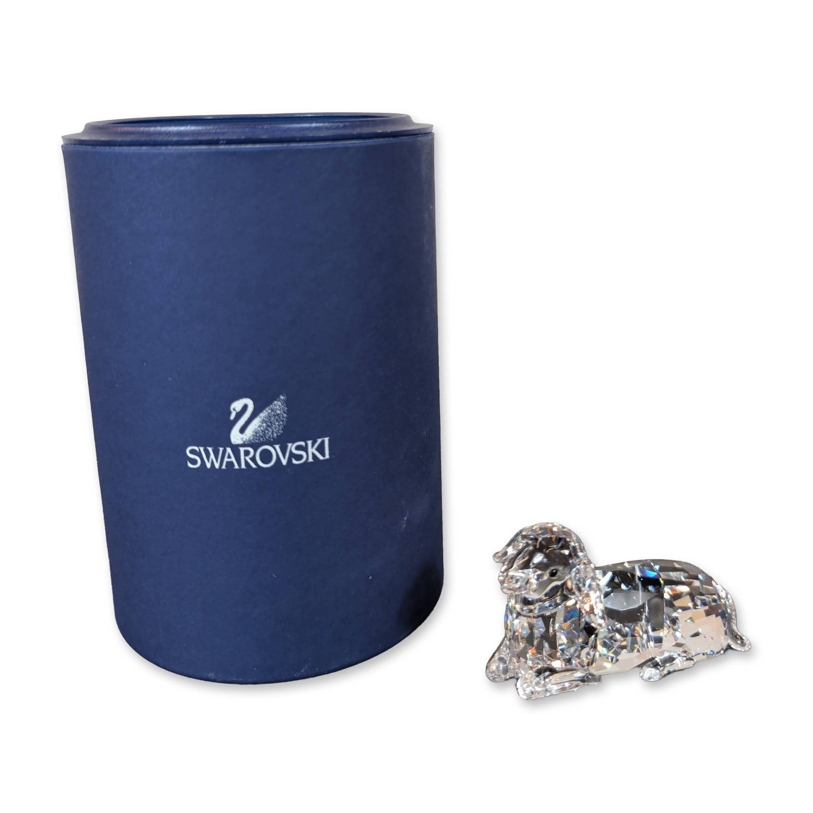 Swarovski Crystal Mother Sheep Lying Figurine: Mother Sheep Lying figurine in faceted clear lead crystal, featuring floppy ears and a crystal tail. Etched with the Swarovski swan logo mark on the rear haunch. Accompanied by original blue cylindric