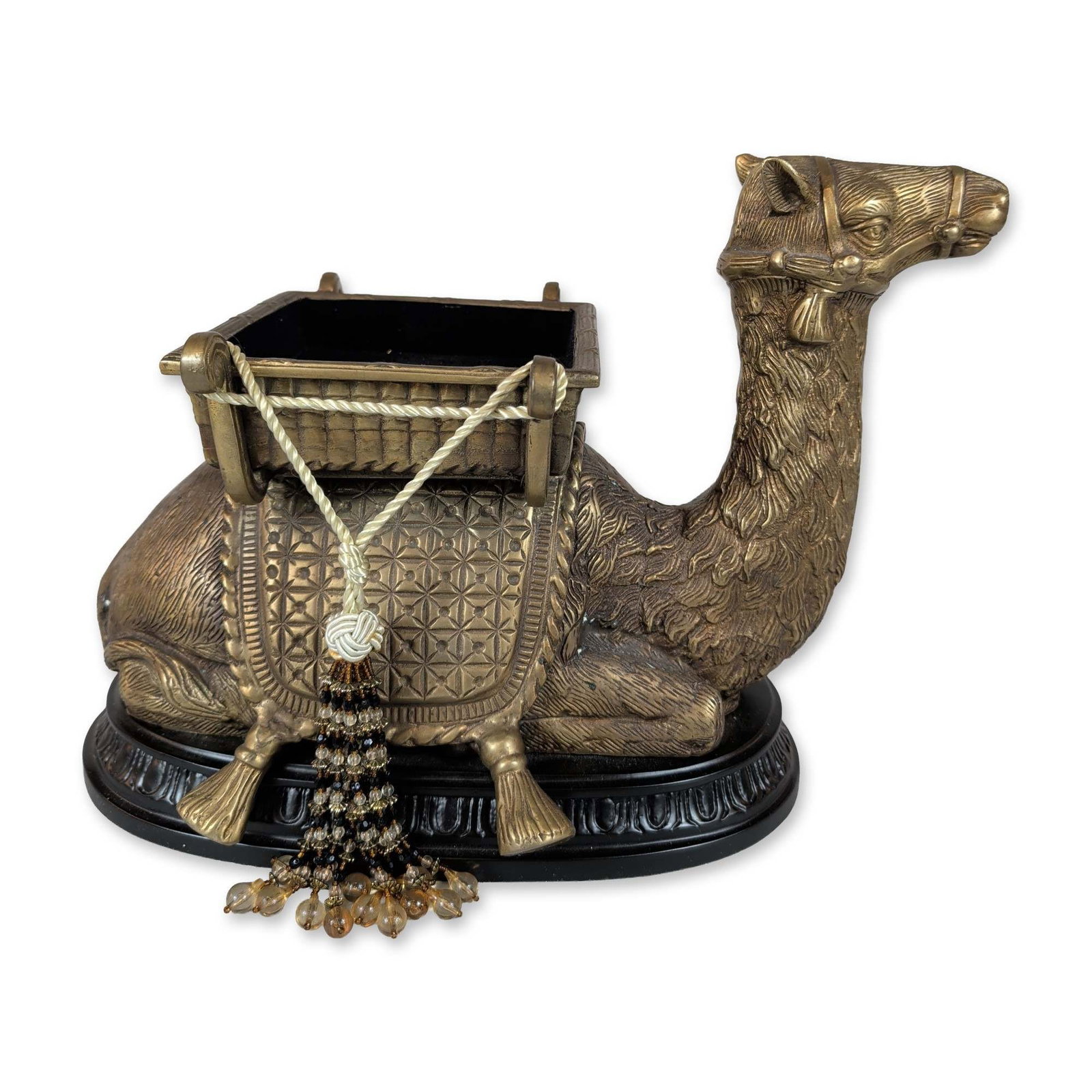 Orientalist Style Golden Tone Brass Camel Sculpture with Saddle Tray: Orientalist style decorative sculpture depicting a seated dromedary camel in golden tone metal. The figure features a textured surface simulating fur and harness details, carrying a rectangular cargo 