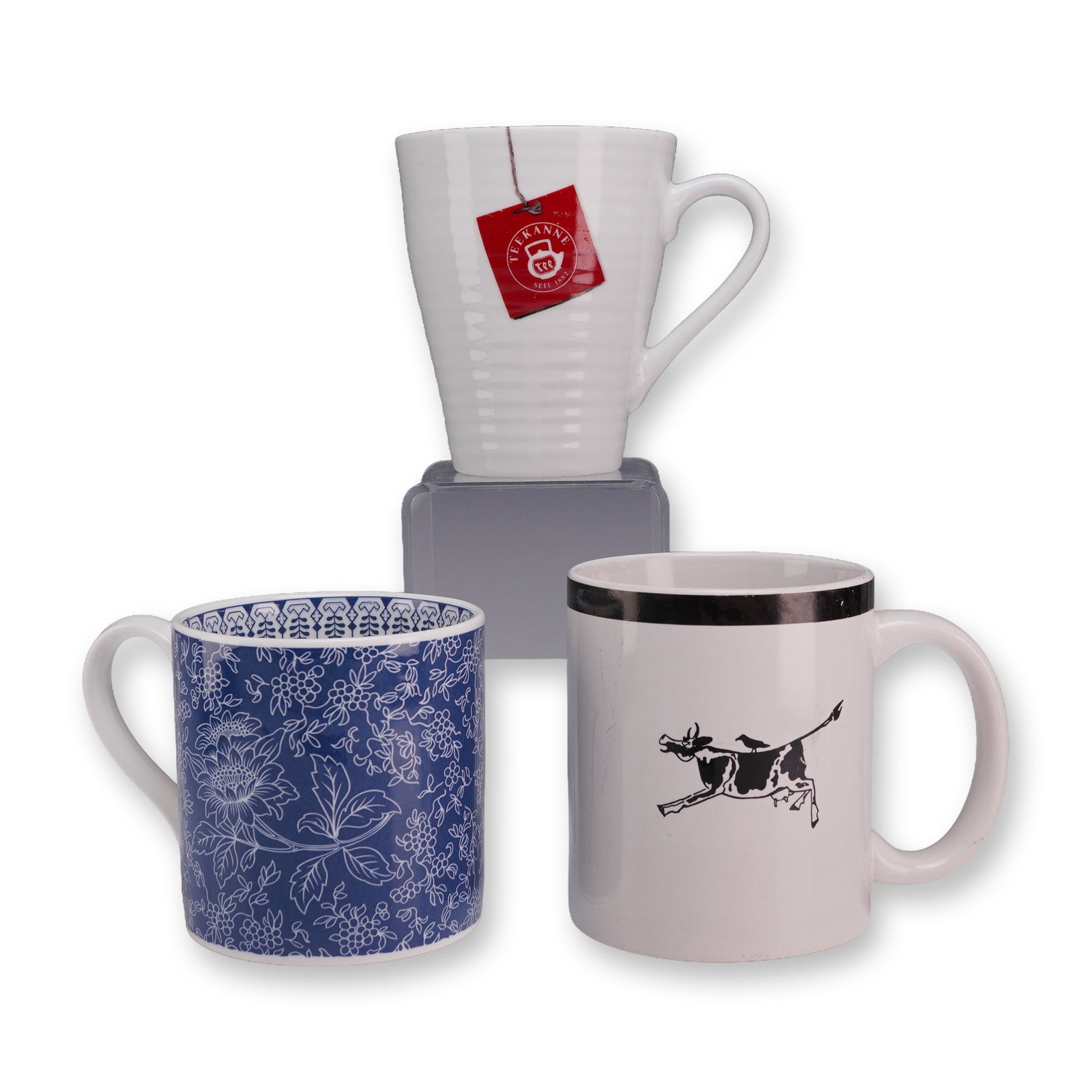 A Trio of Assorted Ceramic Mugs including Wedgwood: A trio of assorted ceramic mugs from various manufacturers. The first mug is a Wedgwood fine earthenware vessel in the Blue Tonquin pattern. It features a cylindrical form with a loop handle, decorate