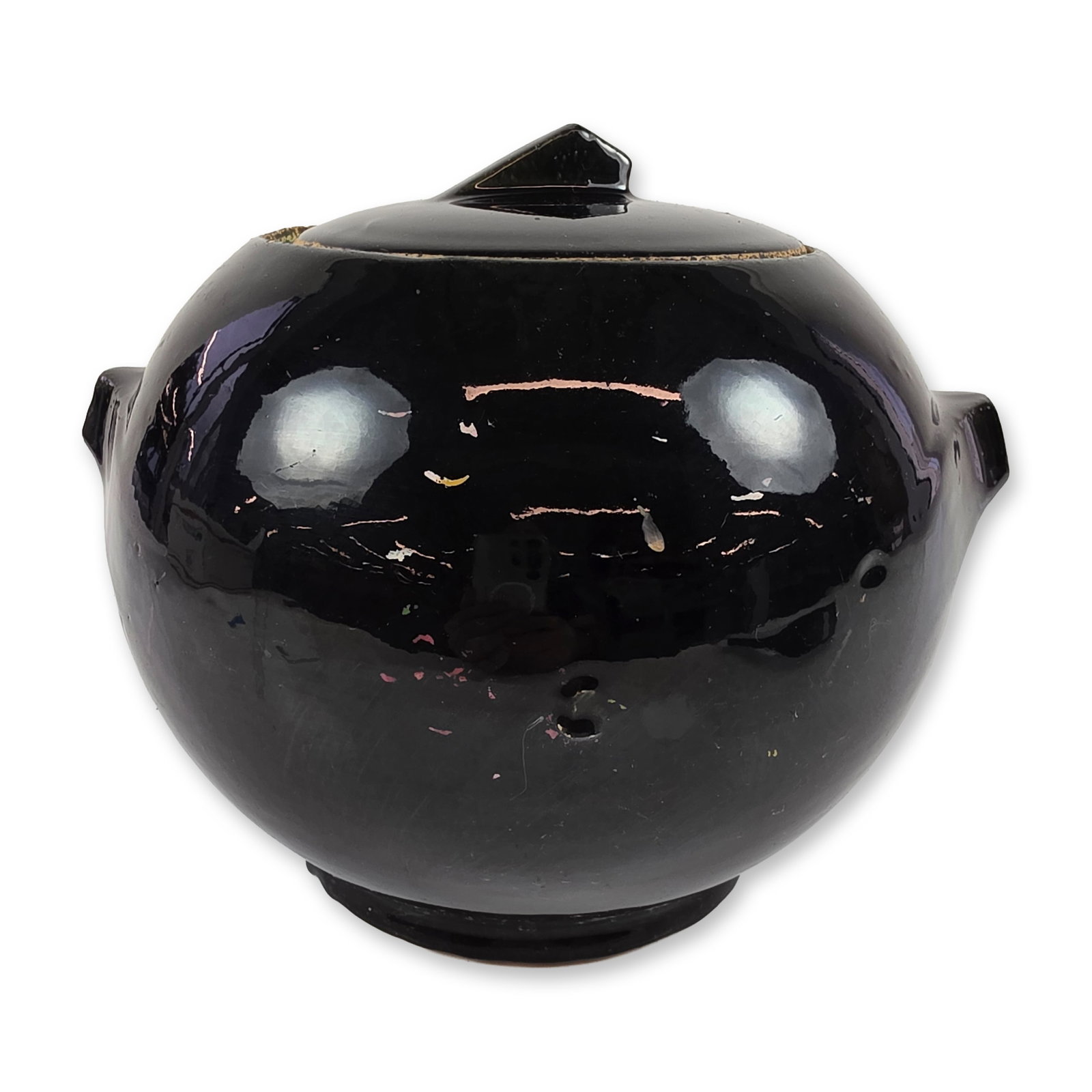 McCoy Black Glazed Cookie Jar: Lidded globular jar in black glazed earthenware, featuring a spherical body with two integral lug handles and a domed lid with a faceted finial. The exterior shows remnants of cold-painted polychrome