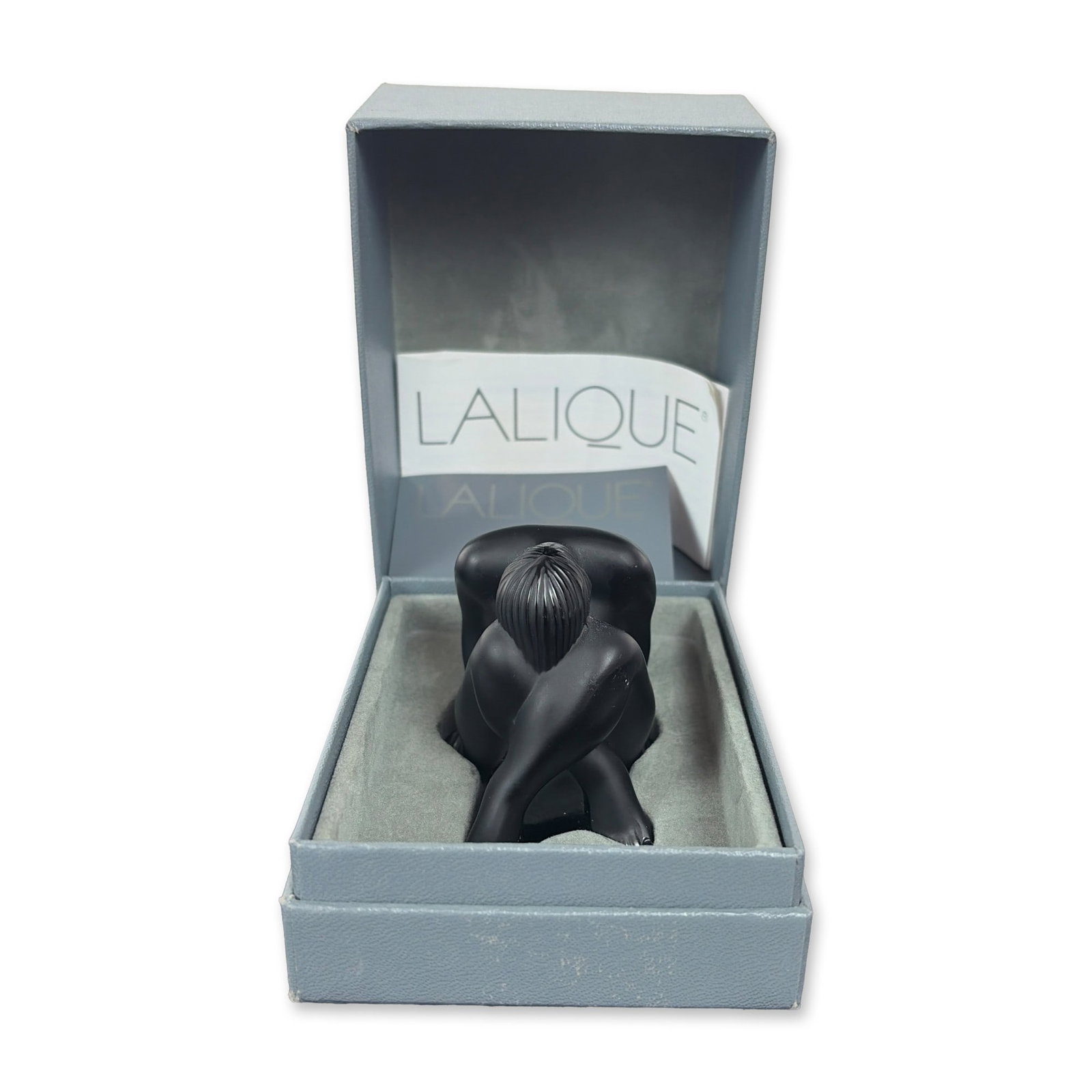 Lalique Black Crystal Seated Nude Figurine: Lalique France seated nude figurine in black satin-finished crystal, titled Nu Assis. The figure is depicted in a crouched pose with head bowed and arms tucked around the legs. Base is hand-signed wit