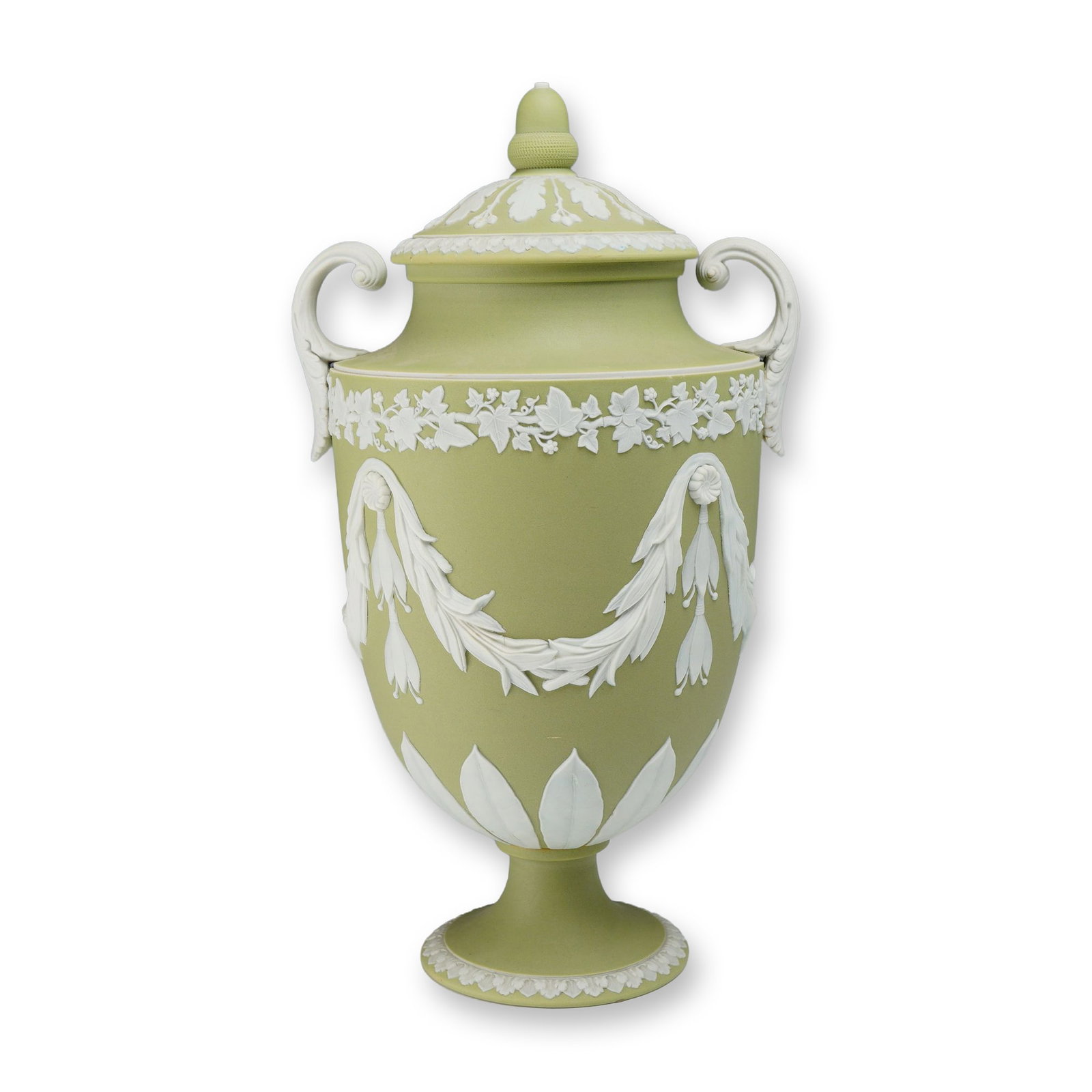 Wedgwood Sage Green Jasperware Lidded Urn: A twin-handled lidded urn of ovoid form crafted from sage green Jasperware with applied white bas-relief decoration. The vessel is set on a pedestal base with a leaf-molded border. The body features w