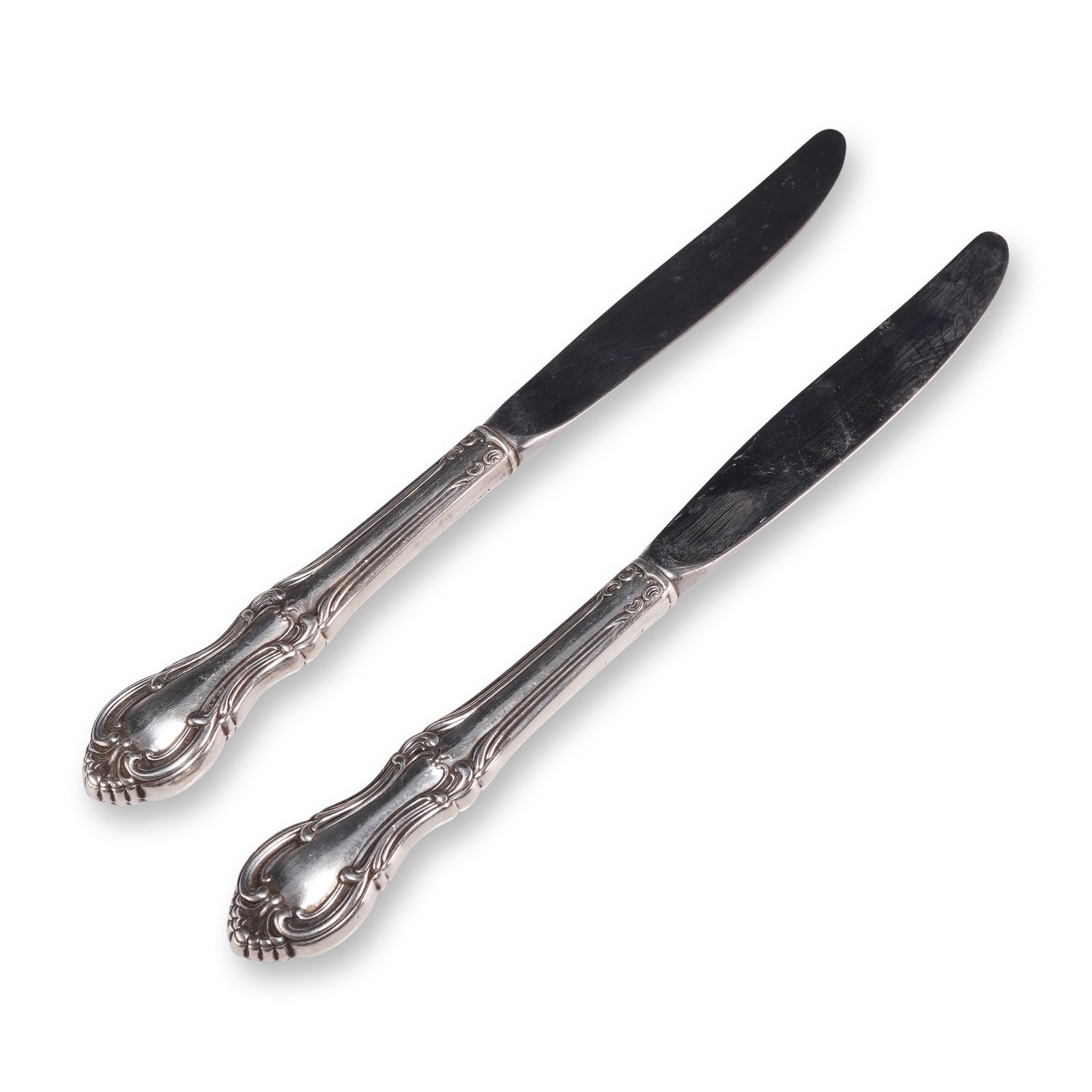 Pair of International Sterling Dinner Knives, Joan of Arc: Pair of International Silver dinner knives in the Joan of Arc pattern. Each knife features a hollow sterling silver handle decorated in a Rococo Revival style with scrolling edges and shell motifs. Fi