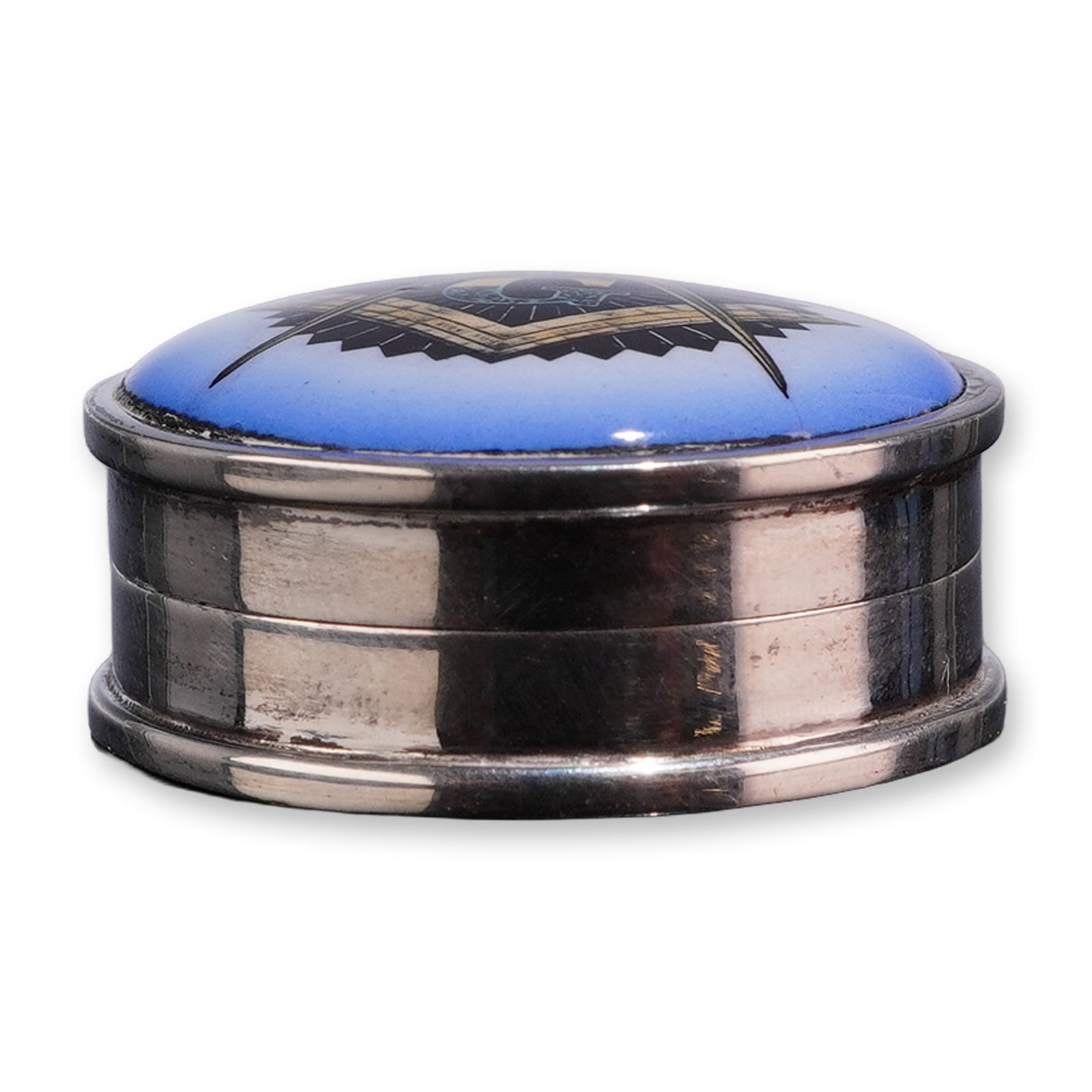 Sterling Silver and Enamel Masonic Pill Box: Sterling silver circular lidded box with a hinged lid. The lid features a Masonic Square and Compasses emblem with a central letter G over a black sunburst, set on a blue guilloche enamel ground. The 