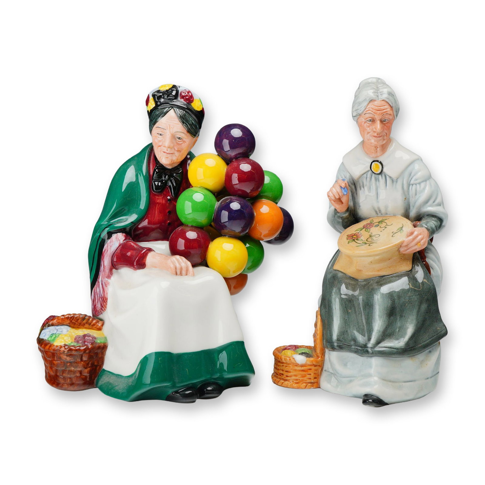 2pc Royal Doulton Porcelain Character Figurines: Royal Doulton. Two glazed porcelain figurines including The Old Balloon Seller (HN 1315) and Embroidering (HN 2855). The Old Balloon Seller depicts an elderly woman seated with a cluster of multi-colo