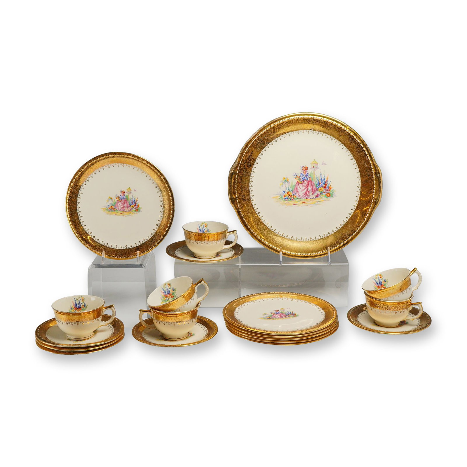 19-Piece Taylor, Smith & Taylor 22K Gold Tea and Dessert Service: Each piece features a central multi-colored transfer-printed motif depicting a woman in Colonial-era dress in a garden setting with a birdhouse, surrounded by heavy 22-karat gold filigree lace borders