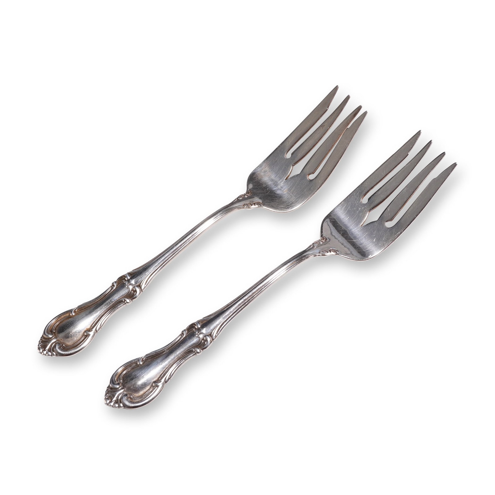 Pair of International Sterling Salad Forks, Joan of Arc: A pair of sterling silver salad forks by the International Silver Company in the Joan of Arc pattern, first introduced in 1940. Each fork is designed in the Rococo Revival style, featuring scrolled bo