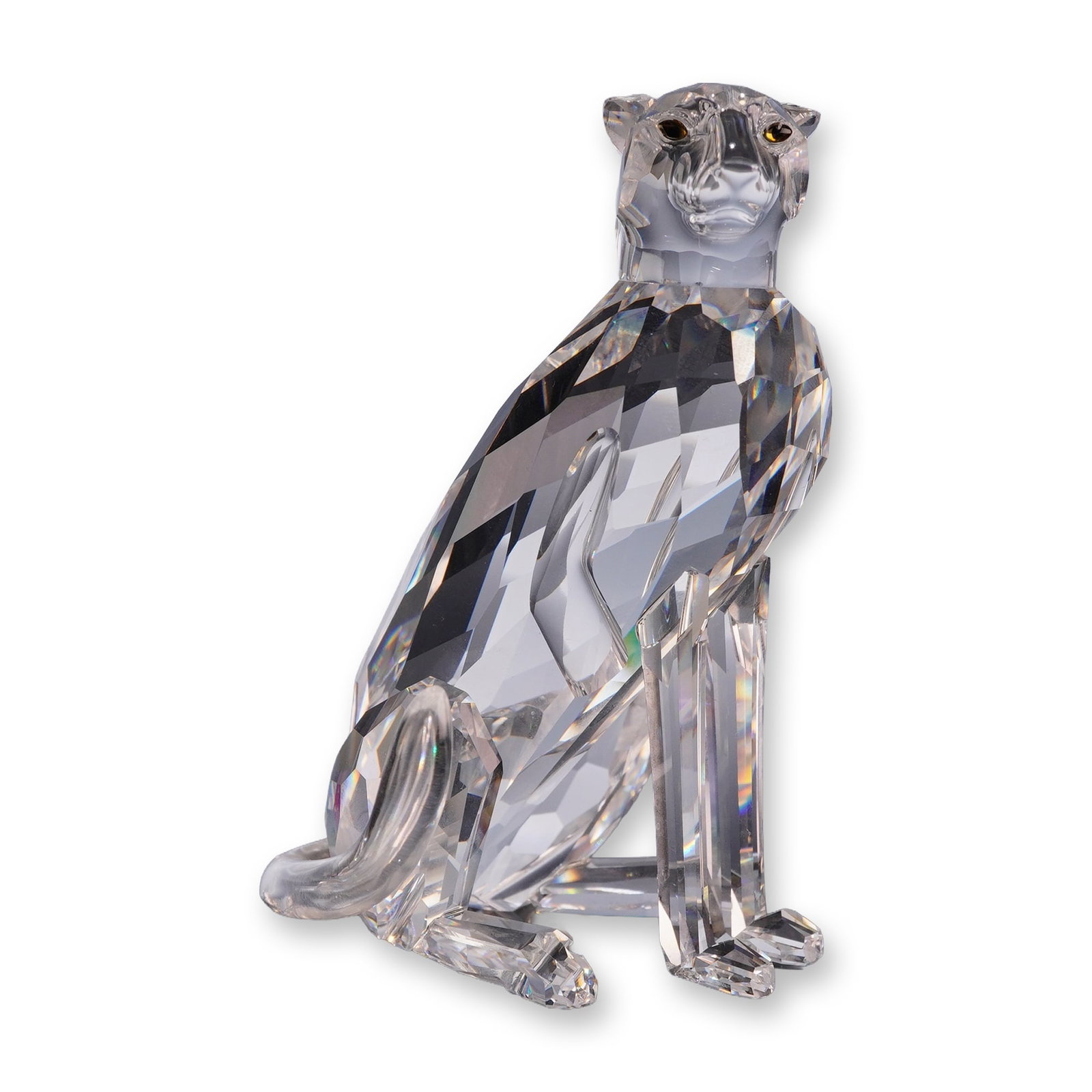 Swarovski Crystal Figurine, Seated Cheetah (low tail): Swarovski faceted clear lead crystal figurine depicting a seated cheetah. The figure features detailed faceting along the body, a smooth curved tail, and inset amber and black crystal eyes. Marked wit