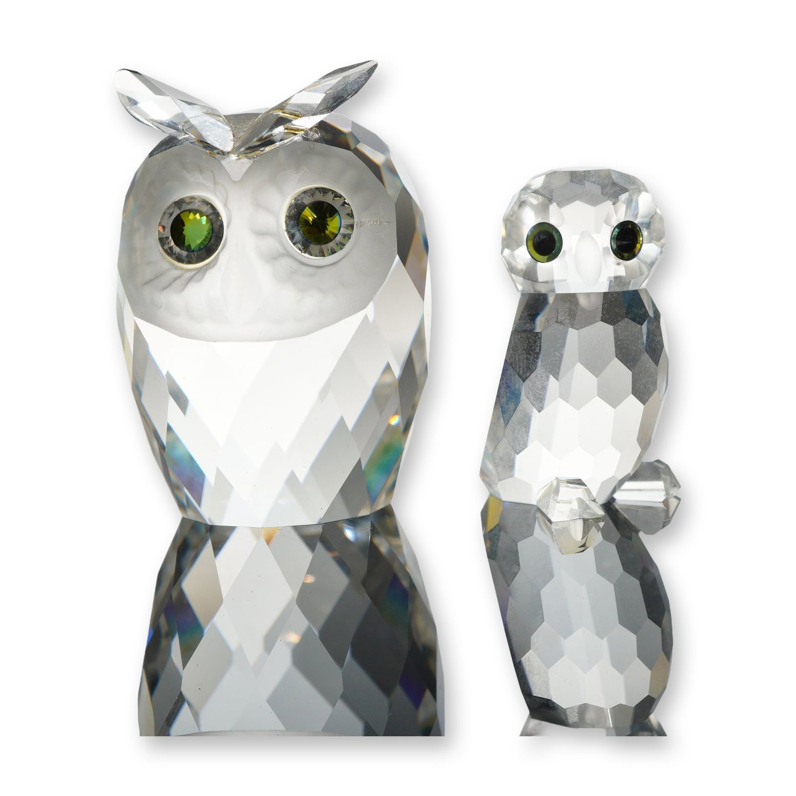 Two Swarovski Silver Crystal Owl Figurines: Swarovski Silver Crystal. A pair of owl figurines in multi-faceted clear lead crystal. The larger owl features a frosted glass face, applied tufted ears, and green and black crystal inset eyes. The sm