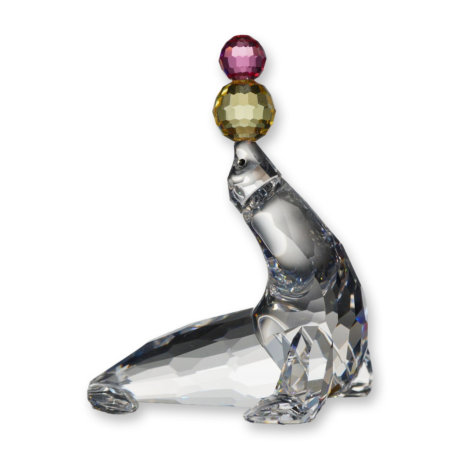 Swarovski Crystal Playing Seal Figurine: Swarovski. Playing Seal figurine, model number 622526, in clear faceted lead crystal. The figurine is depicted in a balancing pose with two stacked, faceted colored crystal spheres on its nose; the lo