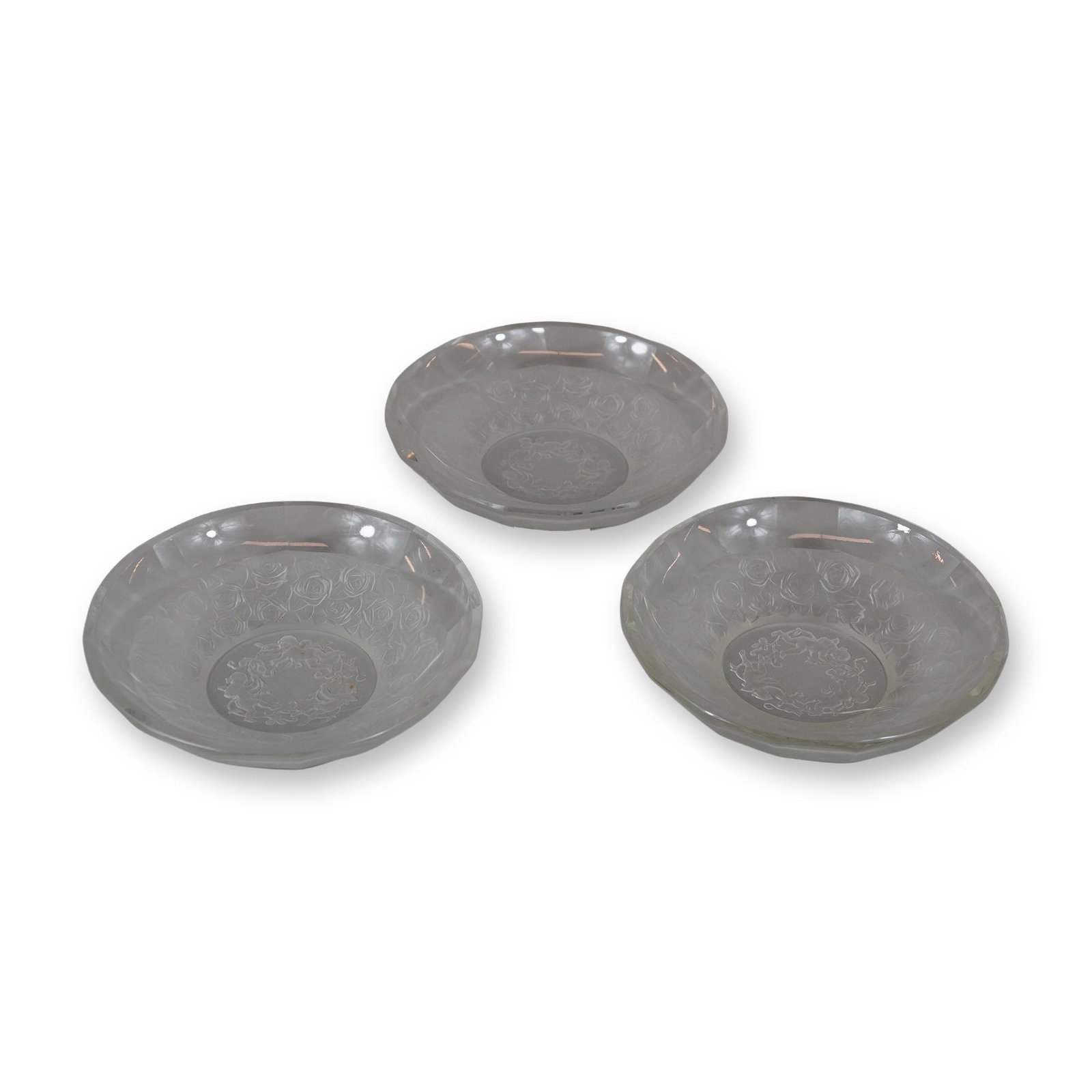 A Set of Three Frosted and Clear Glass Cupids and Roses Pattern Bowls: A matching set of three small glass bowls featuring a combination of clear and frosted finishes. Each bowl is centered with an acid-etched or frosted circular motif depicting three frolicking