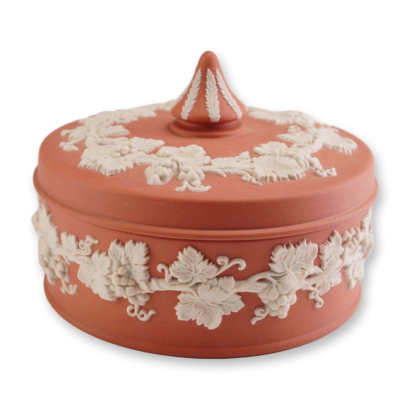 Wedgwood Terracotta Jasperware Lidded Box with White Grapevine Reliefs: A circular lidded box produced by Wedgwood, crafted in terracotta-colored jasperware. The vessel features a matte, unglazed terracotta ground ornamented with white bas-relief sprigged decoration in a 