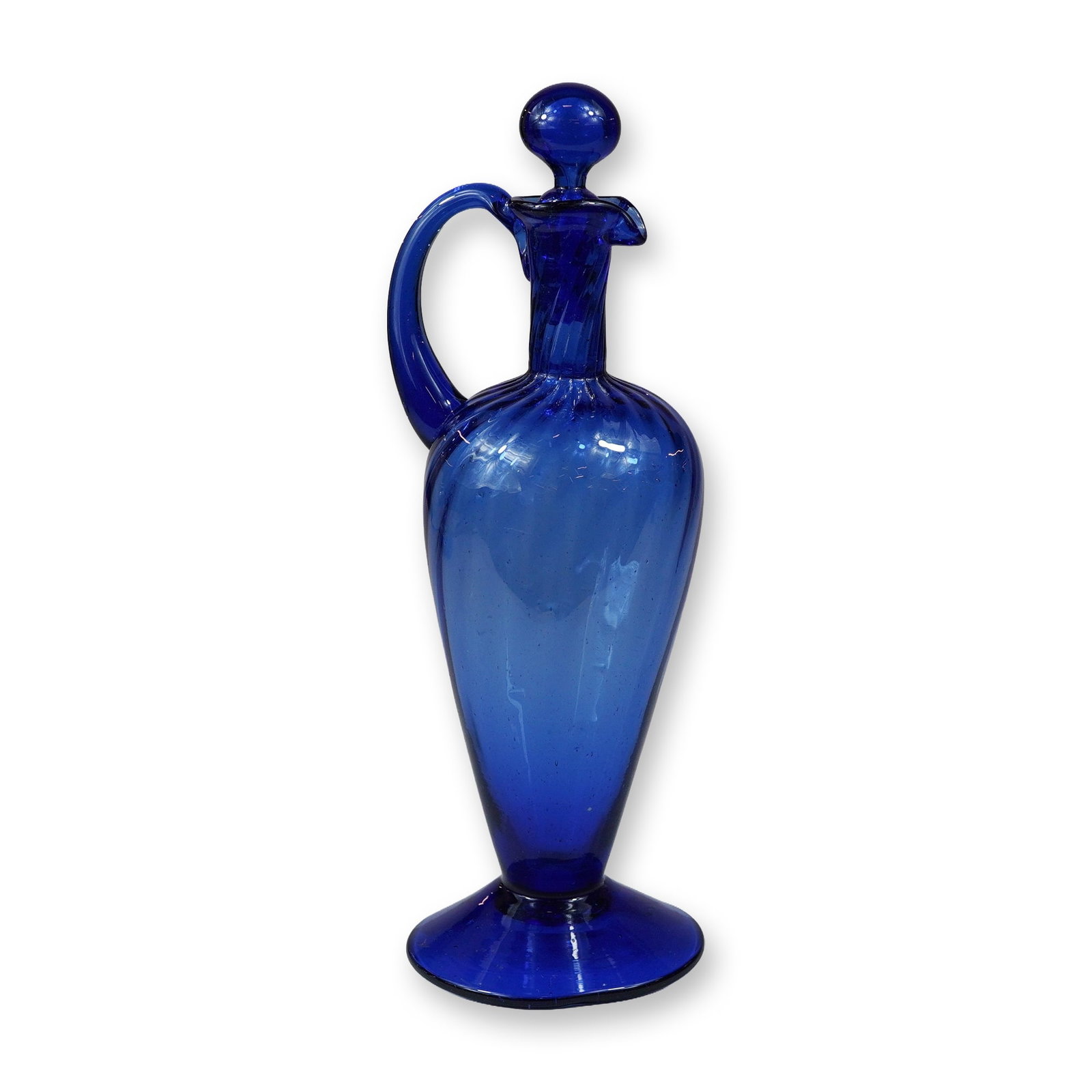 Mid-Century Cobalt Blue Hand-Blown Glass Bottle with Stopper: A hand-blown cobalt blue glass bottle with stopper, designed in a ewer or handled decanter form. The vessel features a tapered body with vertical optic ribbing detailed at the shoulder and neck. It in