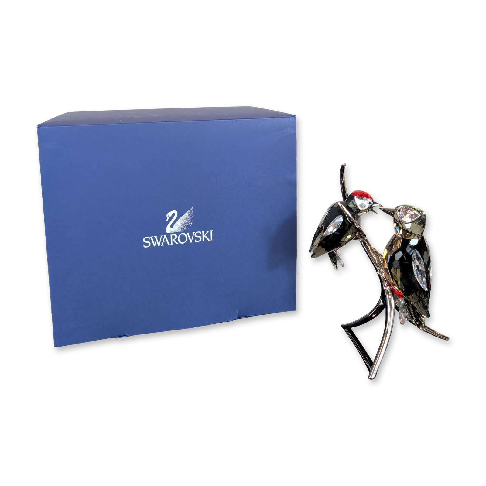 Swarovski Crystal Black Diamond Woodpeckers Figurine: Swarovski. Figurine featuring two woodpeckers in faceted lead crystal, modeled in jet black and grey tones with red crystal accents on the crowns and tails. The birds are perched on a polished silver-