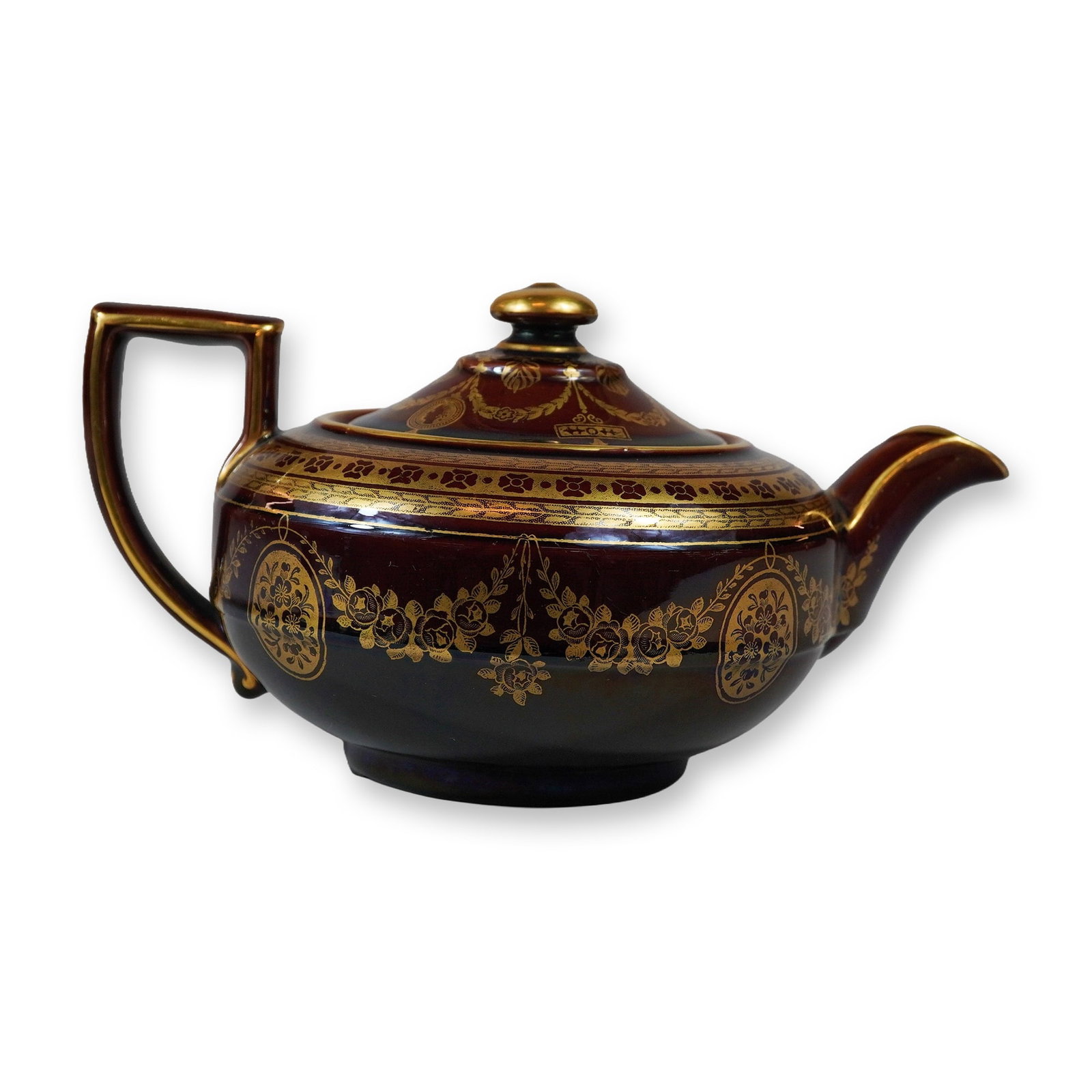 Burgundy Luster Glazed Earthenware Teapot with Heavy Gilt Decoration: This earthenware teapot features a deep burgundy to dark chocolate brown luster glaze with ornate gilt ornamentation. The teapot is designed with a squat, bulbous body, an angular square-shouldered ha