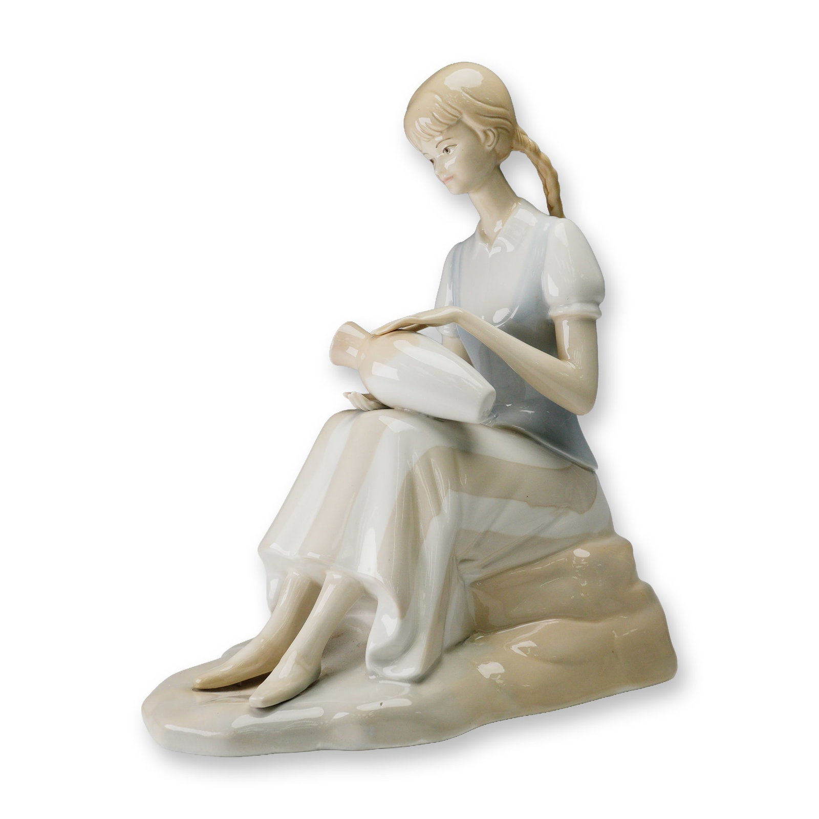 Porceval Spain Porcelain Figurine, Girl with Vase: The figure is crafted in soft pastel tones with a glossy glaze, highlighting delicate details such as the girl's braided hair, serene expression, and flowing dress. She is shown resting on a naturalis