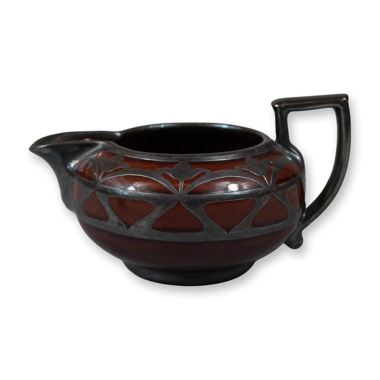 Wedgwood Art Nouveau Earthenware Creamer with Silver Overlay by Hemming Manufacturing Co.: An Art Nouveau earthenware cream pitcher of squat bulbous form featuring a deep mahogany colored treacle glaze. The exterior is decorated with an intricate silver overlay depicting a repeating stylize
