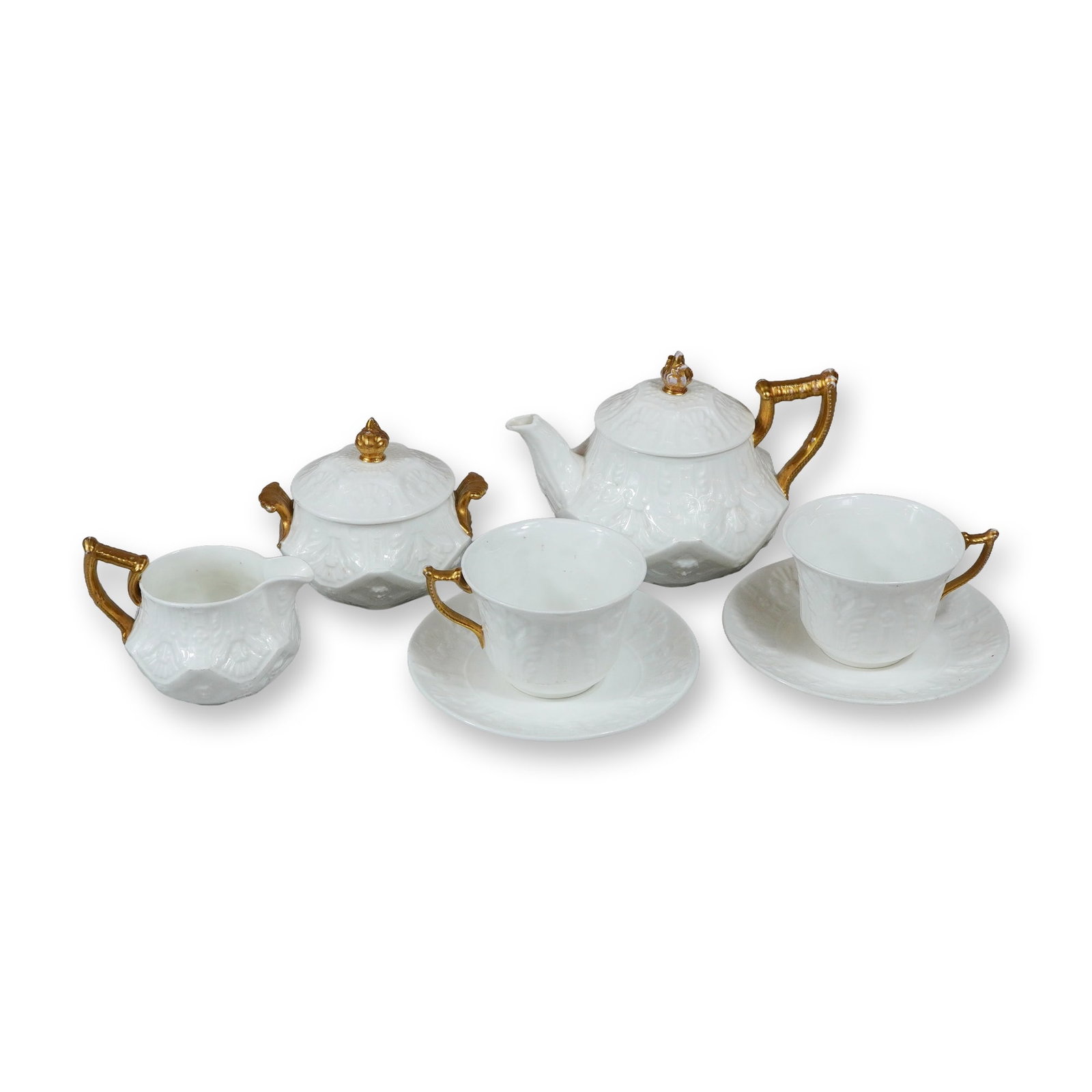 7pc Wedgwood Gilt and White Relief-Molded Bone China Tea Service: A set of bone china tea service items produced by Wedgwood. Each piece features a crisp white body decorated with intricate relief-molded patterns of neoclassical and foliate motifs. The handles, spou