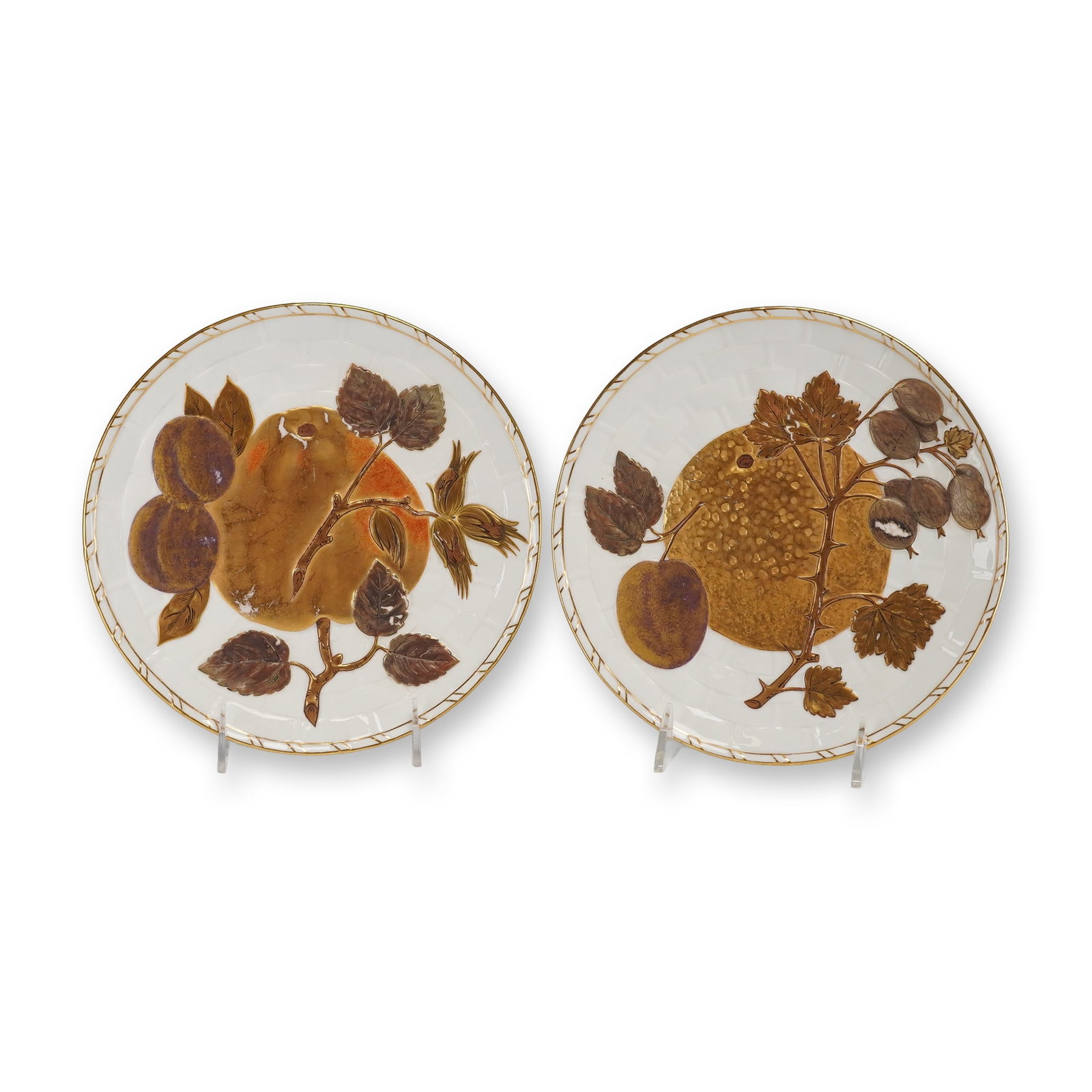 2pc Wedgwood Gilded Fruit Plates: A pair of Wedgwood Gilded Fruit Plates. These circular plates feature a basketweave relief pattern decorated with high-relief molded botanical motifs in various metallic and colored glazes. One plate 