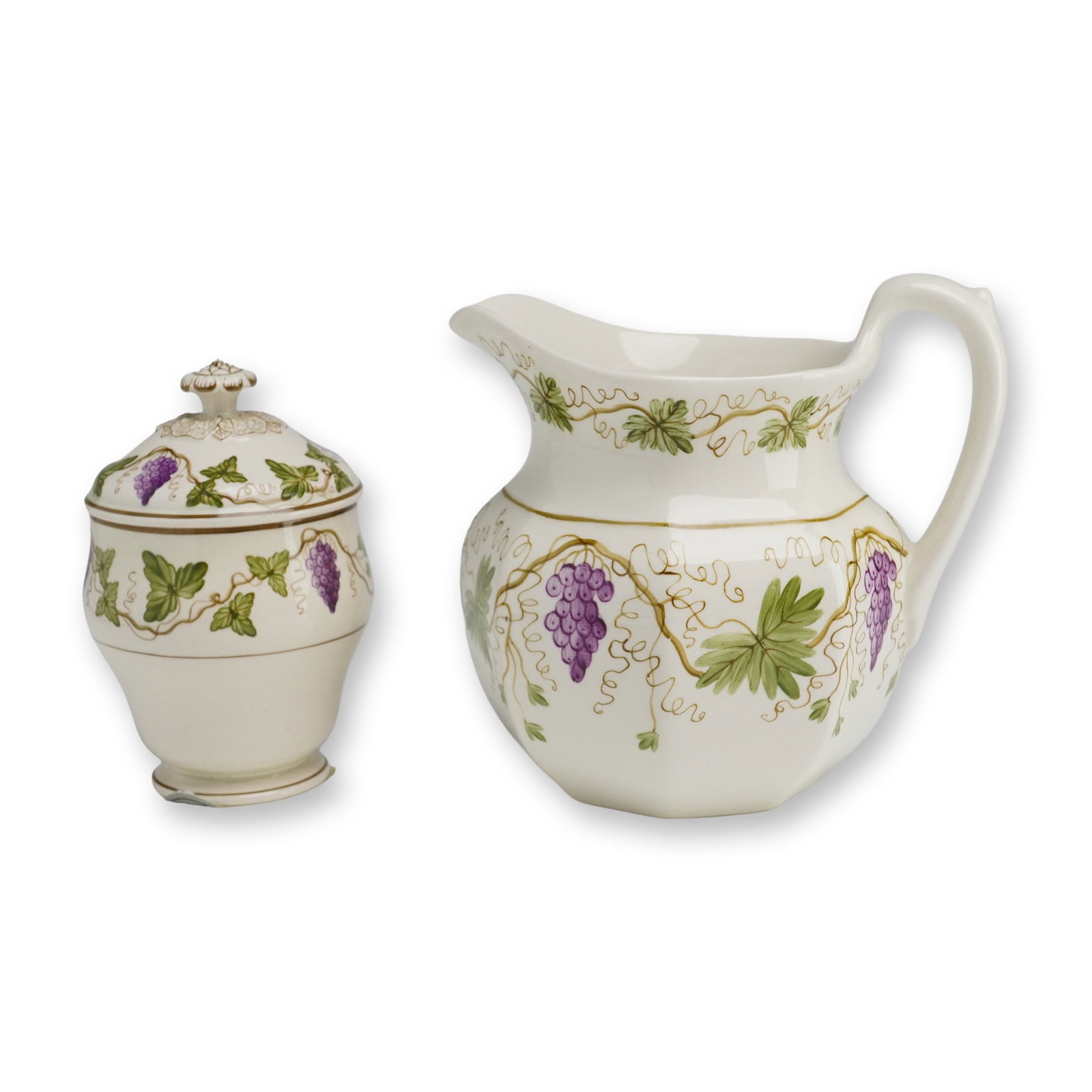 2pc Wedgwood Etruria & Barlaston Grape Motif Creamer and Lidded Sugar Bowl: A Wedgwood creamer and covered sugar bowl, decorated with a purple grapevine and green leaf motif on a cream ground. The sugar bowl lid is surmounted by a flower-form finial. Each piece is marked Wedg