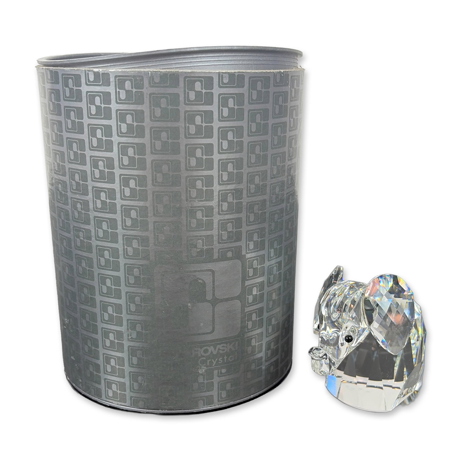Swarovski Silver Crystal Faceted Elephant Figurine: Swarovski stylized elephant that features a faceted body and ears, a curved trunk, and a coiled metal tail. Accented with small black crystal eyes. Bears an etched Swarovski logo mark on the underside