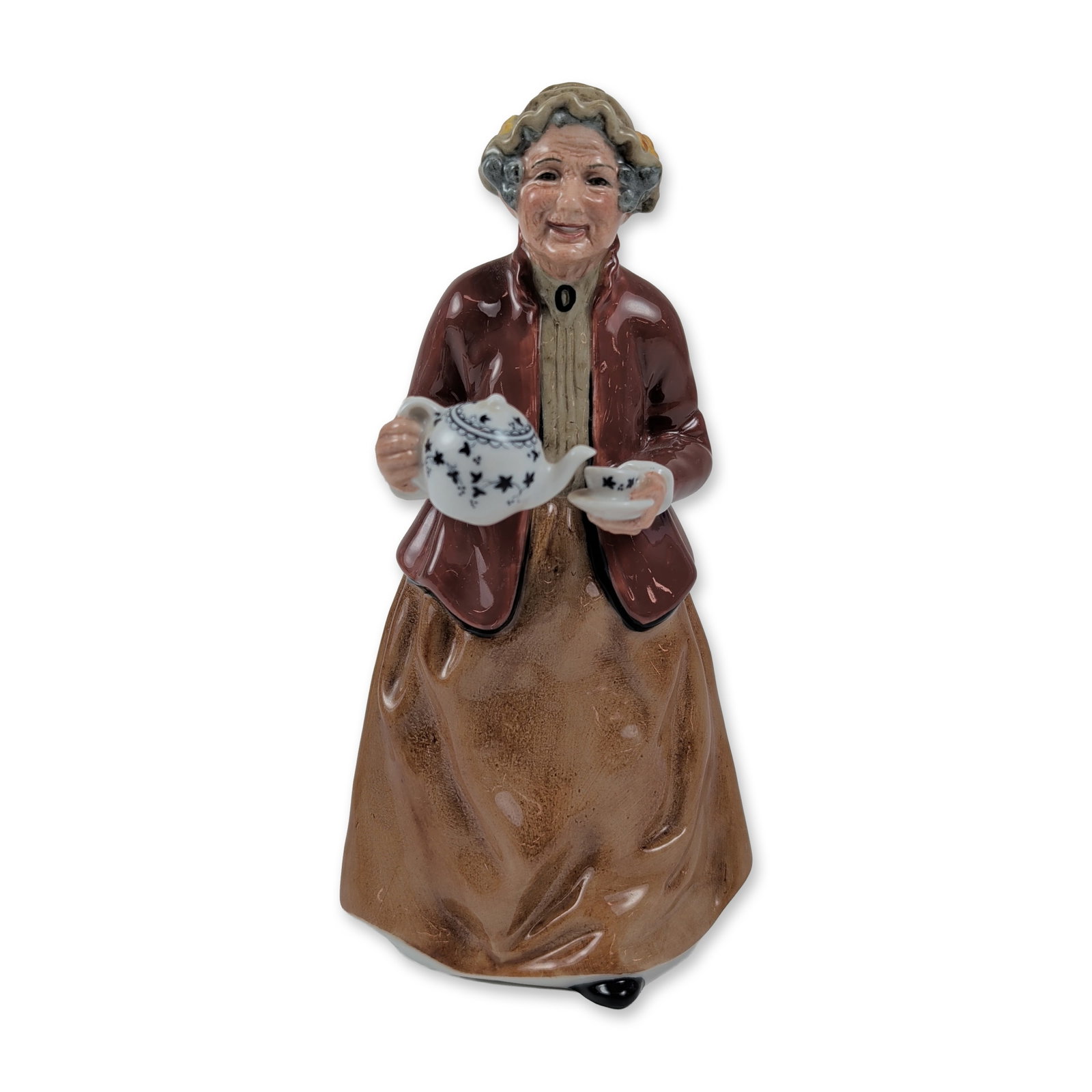 Royal Doulton Teatime Porcelain Figurine HN2255: The hand-painted figure depicts an elderly woman in traditional dress, featuring a maroon jacket over a beige blouse and a full brown skirt. She is shown pouring tea from a blue and white patterned te