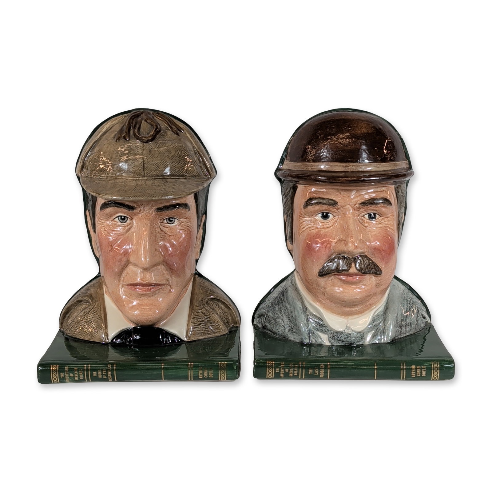 Pair of Royal Doulton Sherlock Holmes and Watson Bookends: Royal Doulton glazed ceramic bookends depicting literary figures Sherlock Holmes and Dr. Watson. The Sherlock Holmes figure (D7038) is modeled in a tan coat and deerstalker hat, set against a green bo