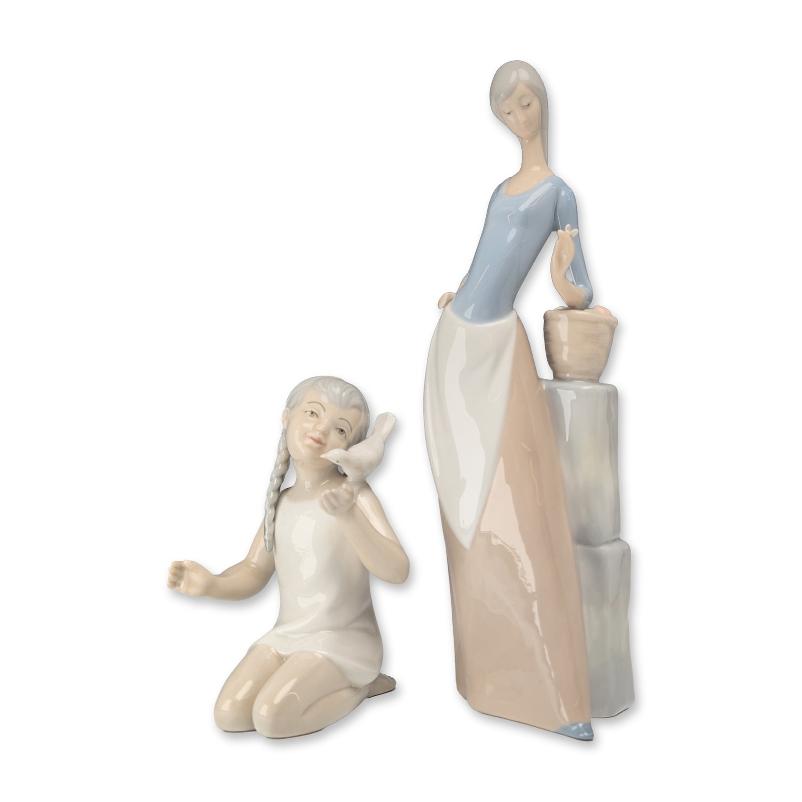 2pc Spanish Glazed Porcelain Figurines, Nao by Lladro and Porceval: Spanish, 20th century. Two glazed porcelain figurines by Nao by Lladro and Porceval. One figurine depicts a standing woman wearing a blue bodice, and taupe skirt, standing beside a low square pillar w