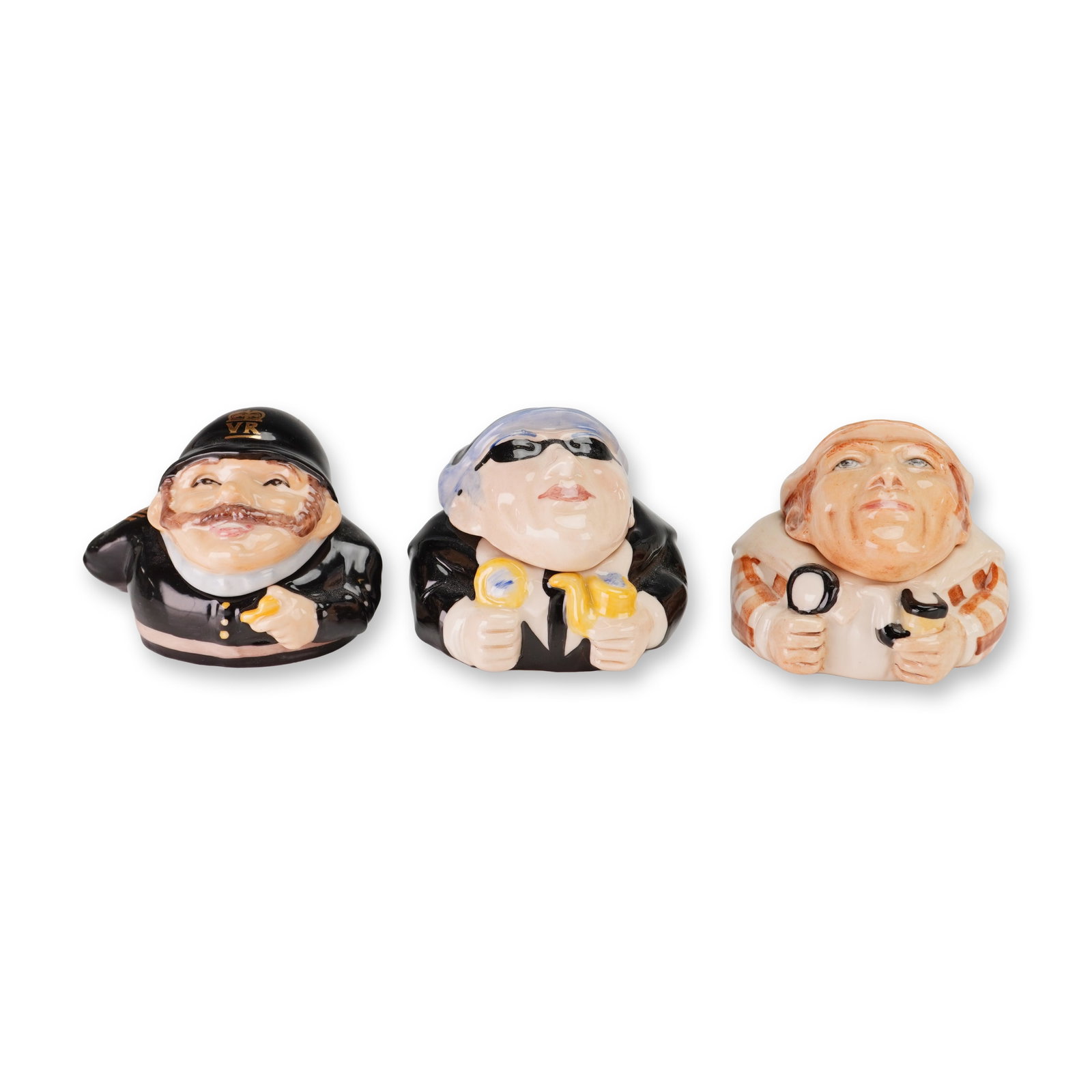 3pc Kevin Francis Ceramic Face Pots, British Bobby and Sherlock Holmes: A trio of character-themed glazed ceramic trinket boxes by Kevin Francis, marketed as Face Pots. The collection features three distinct designs: a British Bobby wearing a black police helmet with a VR