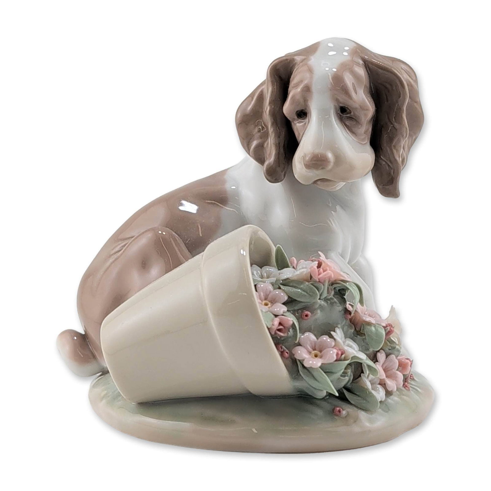 Lladro It Wasnt Me Porcelain Figurine 7672: Lladro glazed porcelain figurine titled It Wasnt Me!, model number 7672. The piece depicts a seated spaniel puppy in brown and white tones positioned beside an overturned flowerpot. The pot contains a