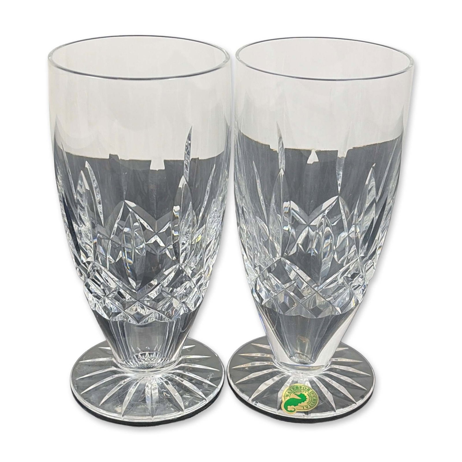 Pair of Waterford Lead Crystal Lismore Footed Iced Tea Glasses: Heavy lead crystal construction featuring a central band of diamond cuts flanked by vertical wedge cuts. The base of each glass exhibits a multi-point radial star cut. Both pieces bear the acid-etched